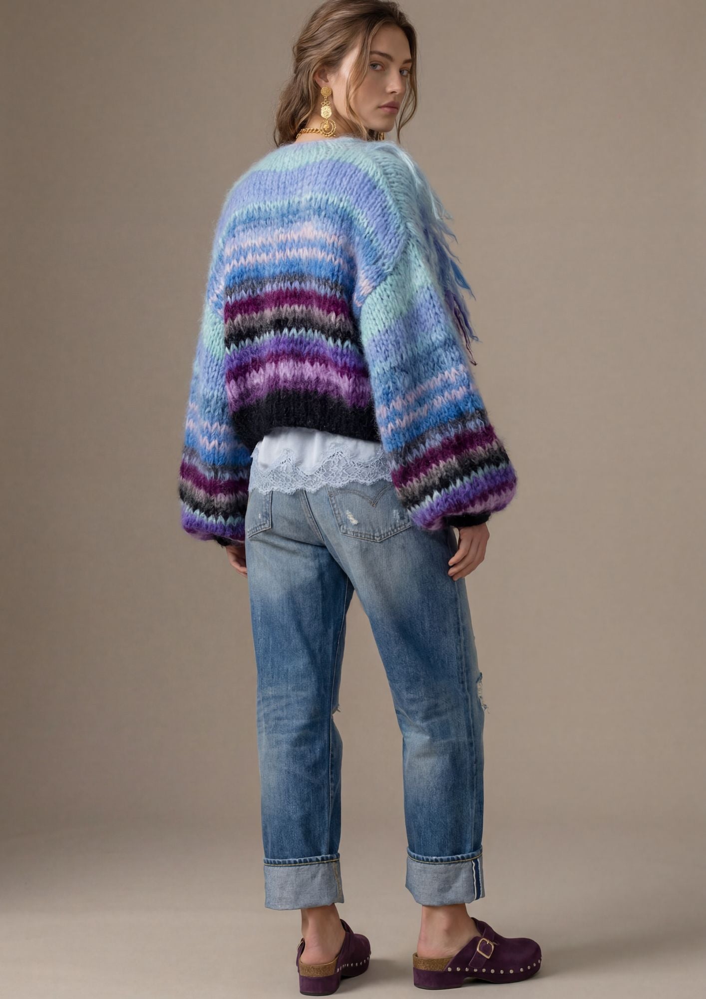 Woman wearing a colorful striped sweater and blue jeans against a beige background
