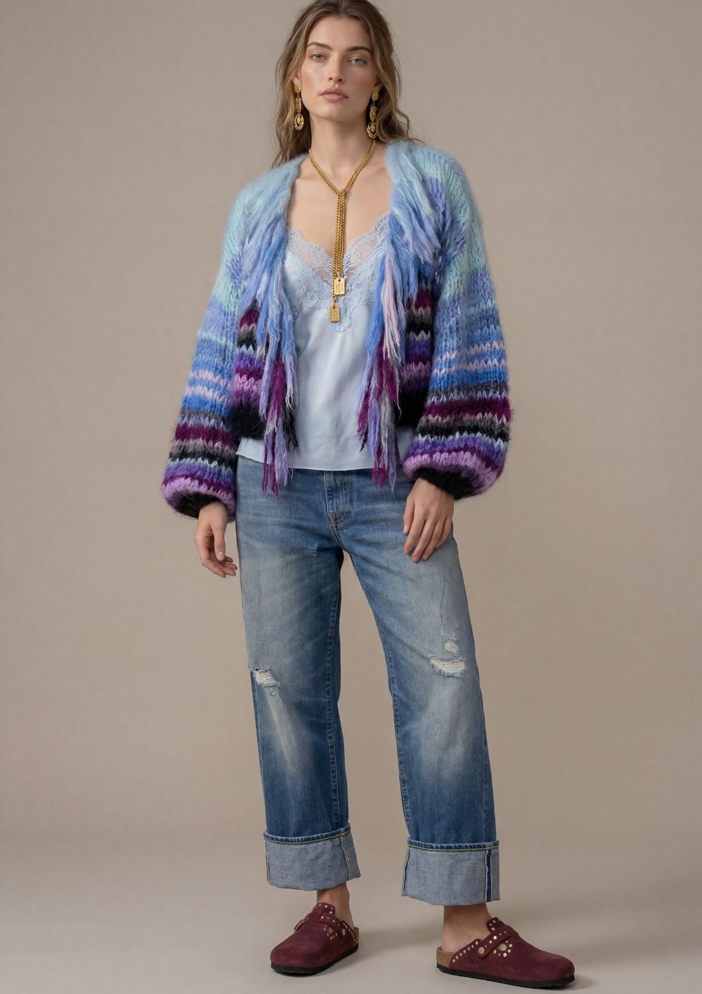 Woman wearing a colorful cardigan, white top, blue jeans, and maroon shoes against a beige background