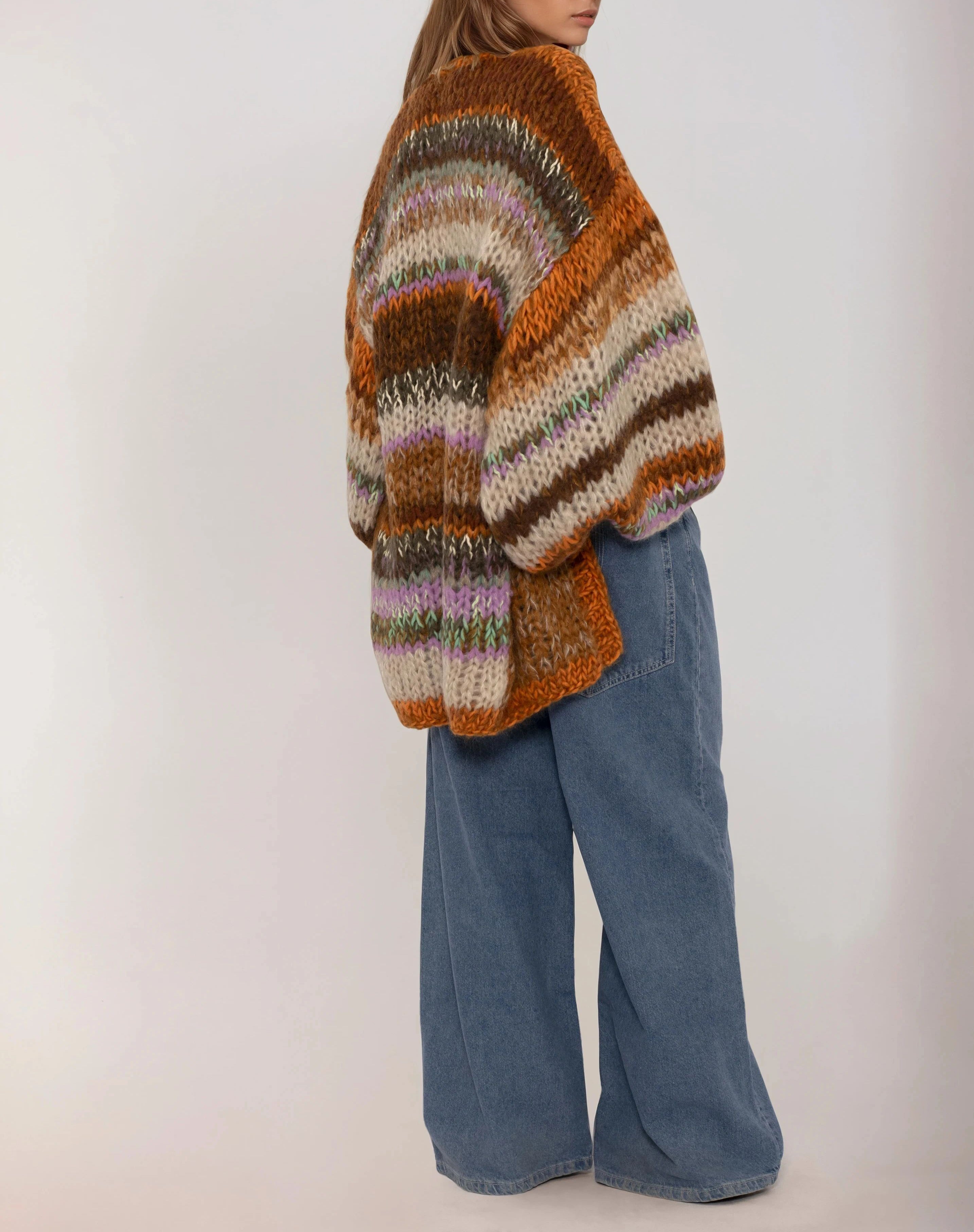 Person wearing a multicolored handknitted sweater and blue jeans on a plain background