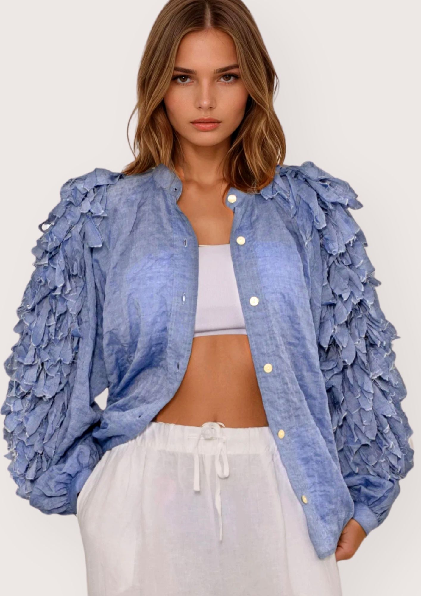 Woman wearing a blue ruffled jacket over a white top and pants on a light gray background