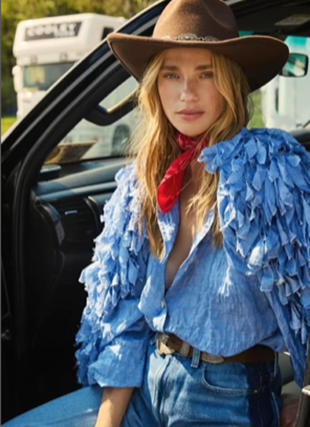 Woman in a cowboy hat and blue jacket sitting in a vehicle.