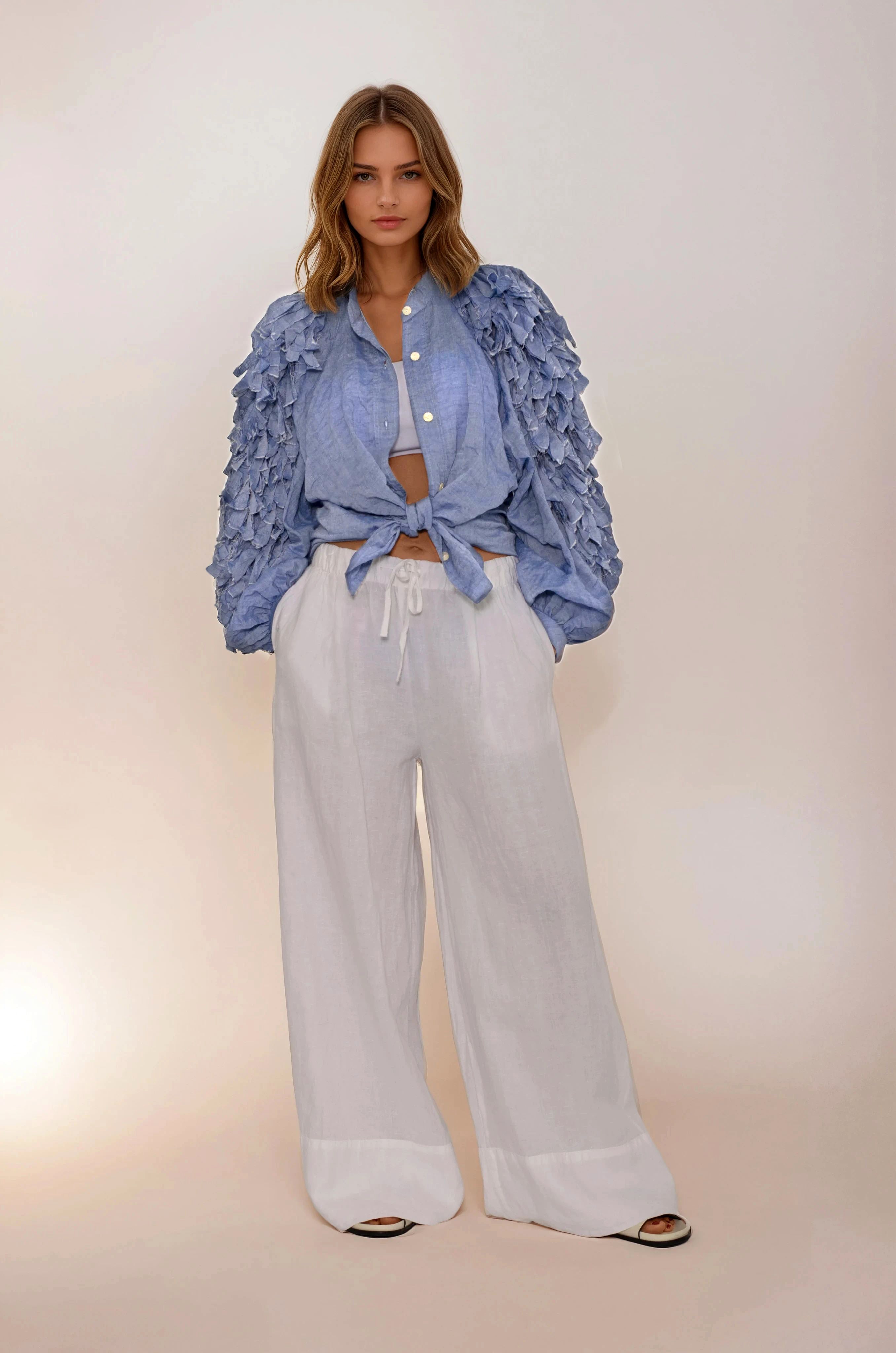 Woman wearing a blue ruffled blouse and white pants on a beige background
