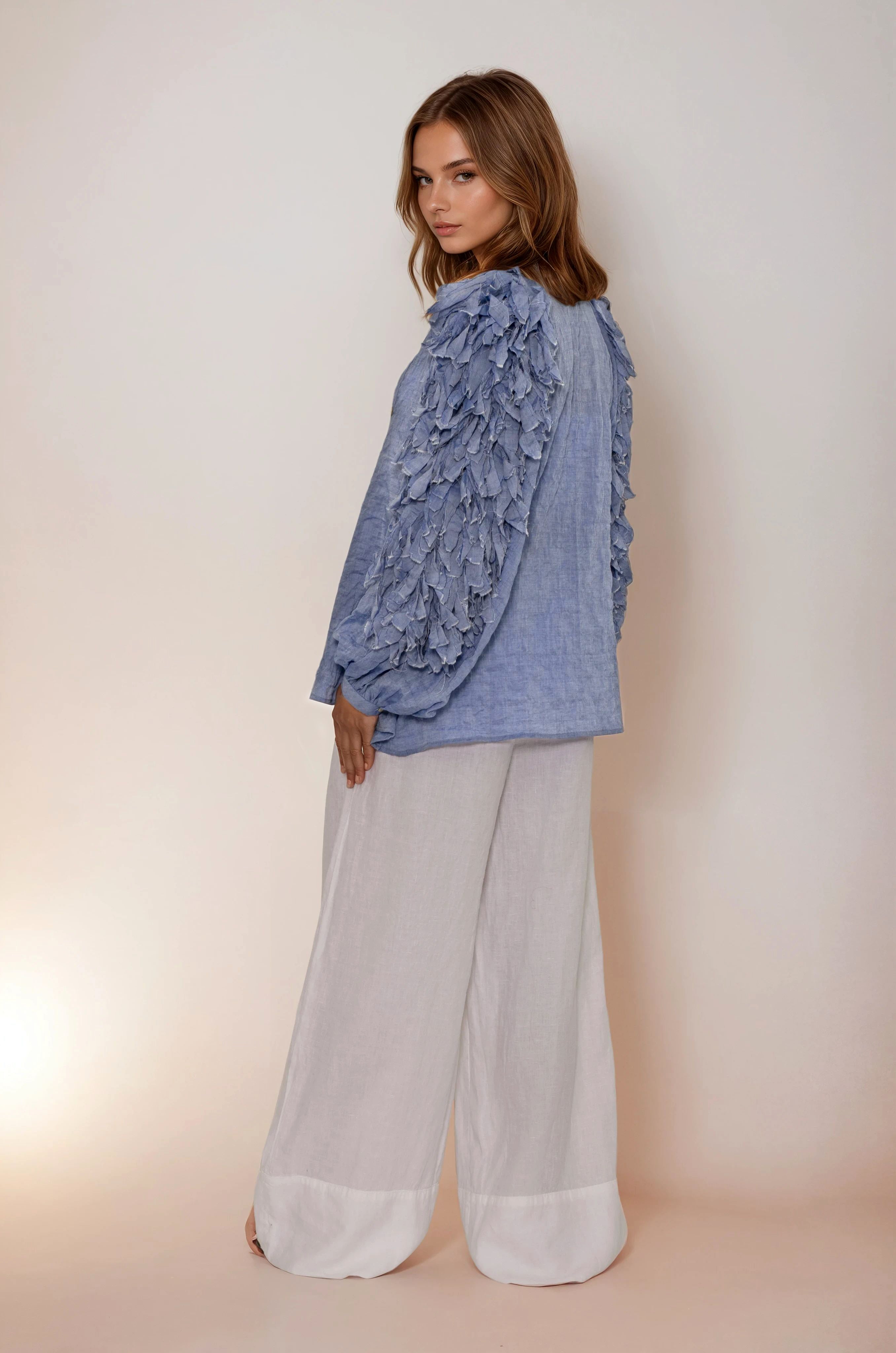 Woman wearing a blue floral Claramonte top and light gray pants on a plain background