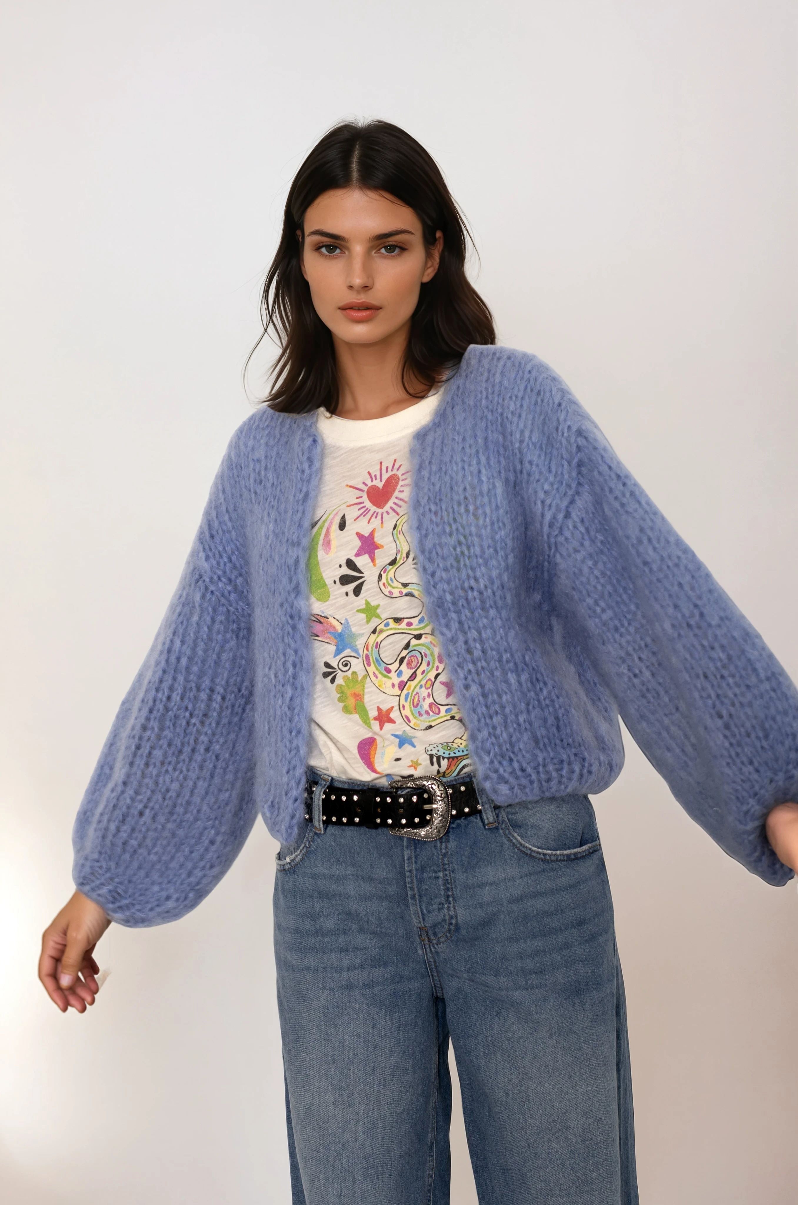 Woman wearing a blue cardigan over a colorful shirt with jeans on a white background