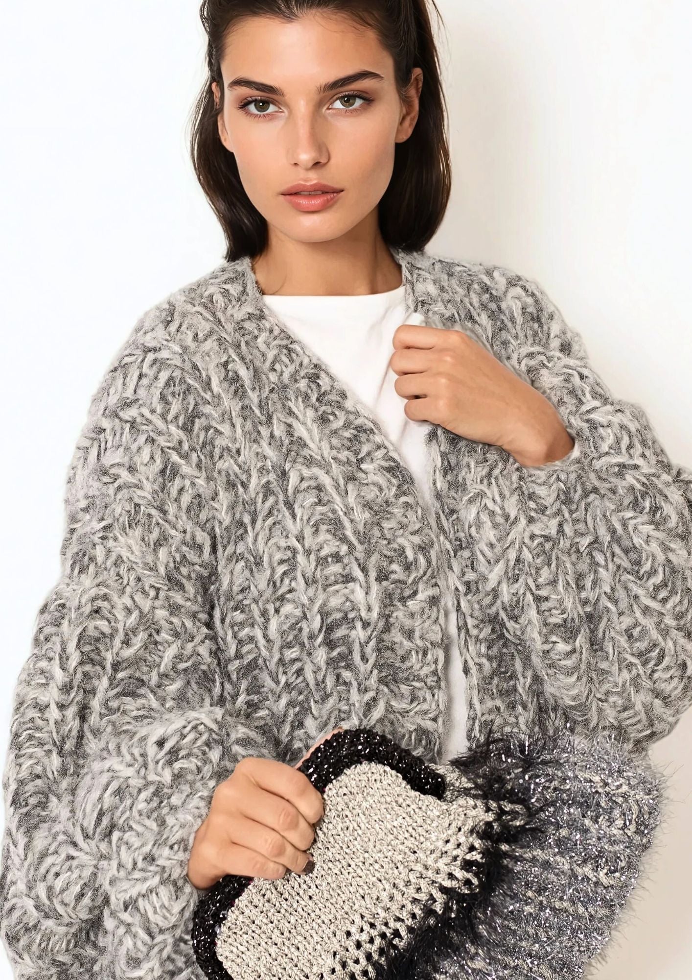 Beutiful girl with dark hair in white t shirt and grey melange handknitted oversized luxury mohair cardigan and sparkling handcrocheted Nadia dafri bag