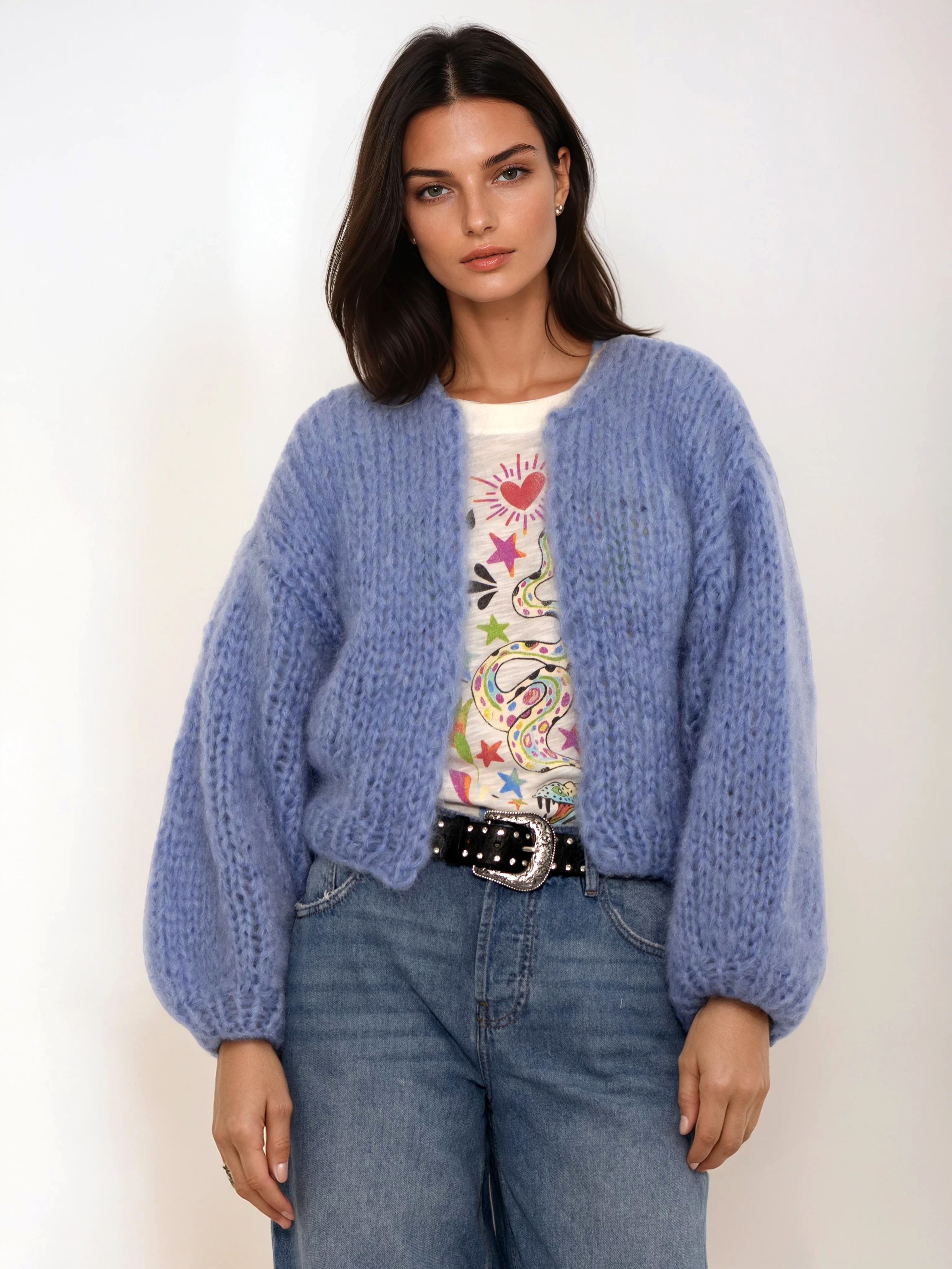 Woman wearing a blue cardigan over a colorful shirt with jeans on a white background