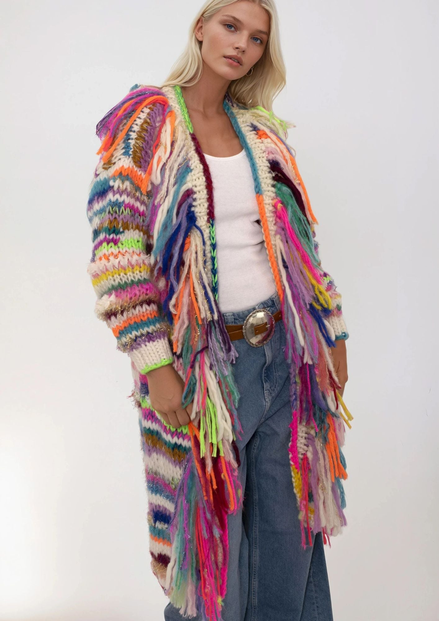 Woman wearing a colorful, handknitted cardigan with fringes against a white background