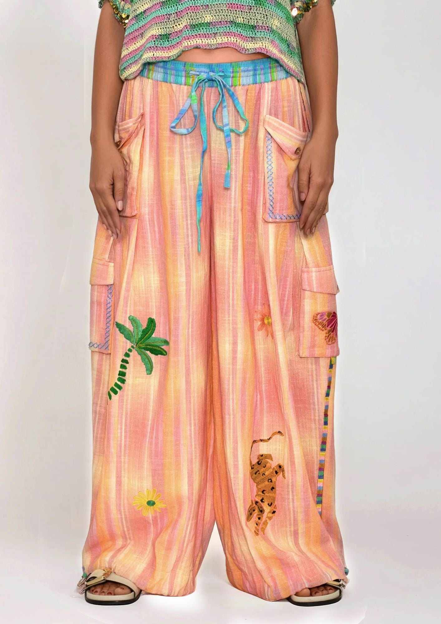 Person wearing colorful pants with floral and leaf embroideries on a white background