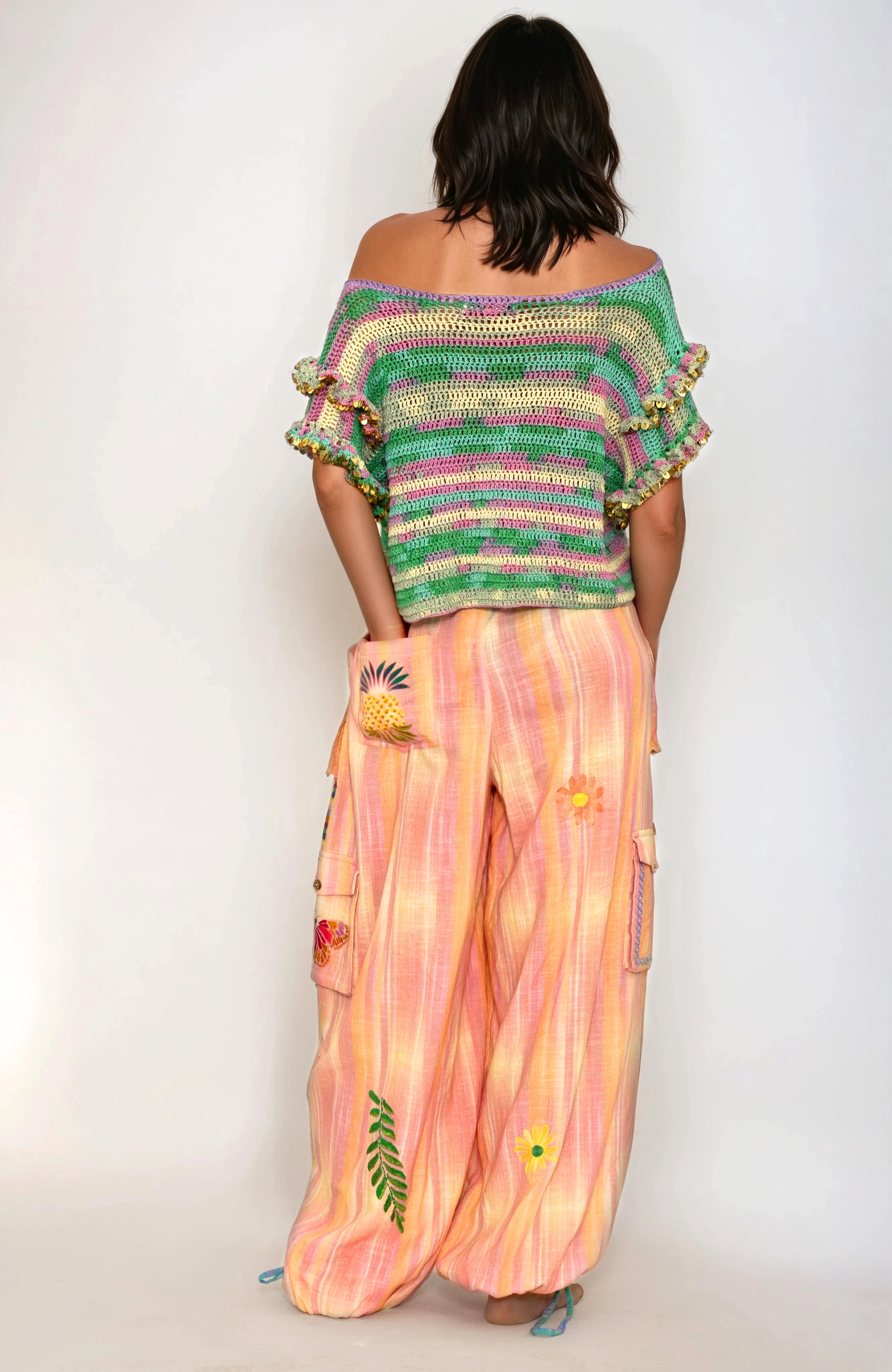Woman wearing a colorful off-shoulder top and pink pants with pineapple designs on a white background