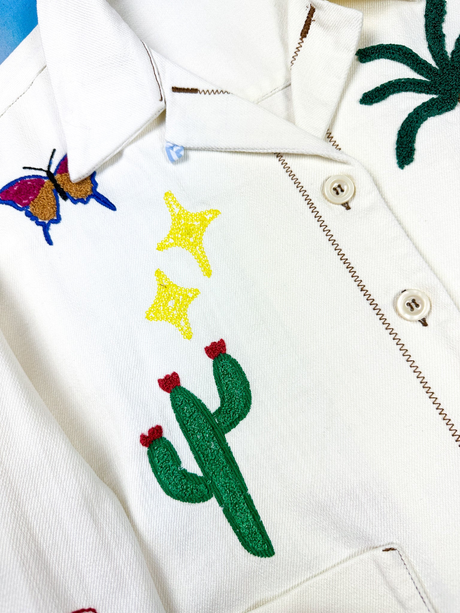 Detail of a white shirt with cactus, stars, butterfly and palm leafs