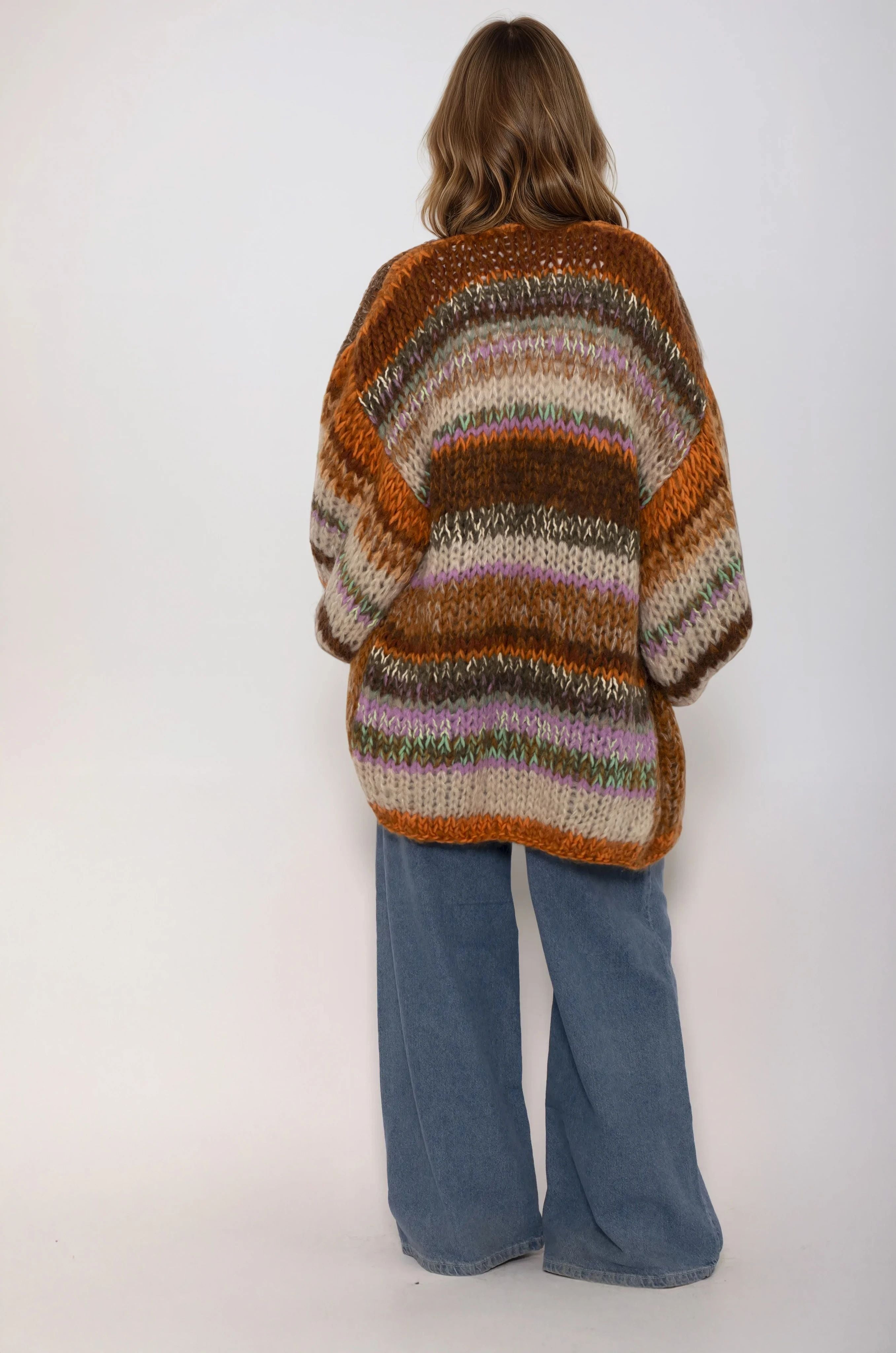 Person wearing a multicolored striped handmade sweater in brown orange beige and blue jeans on a white background