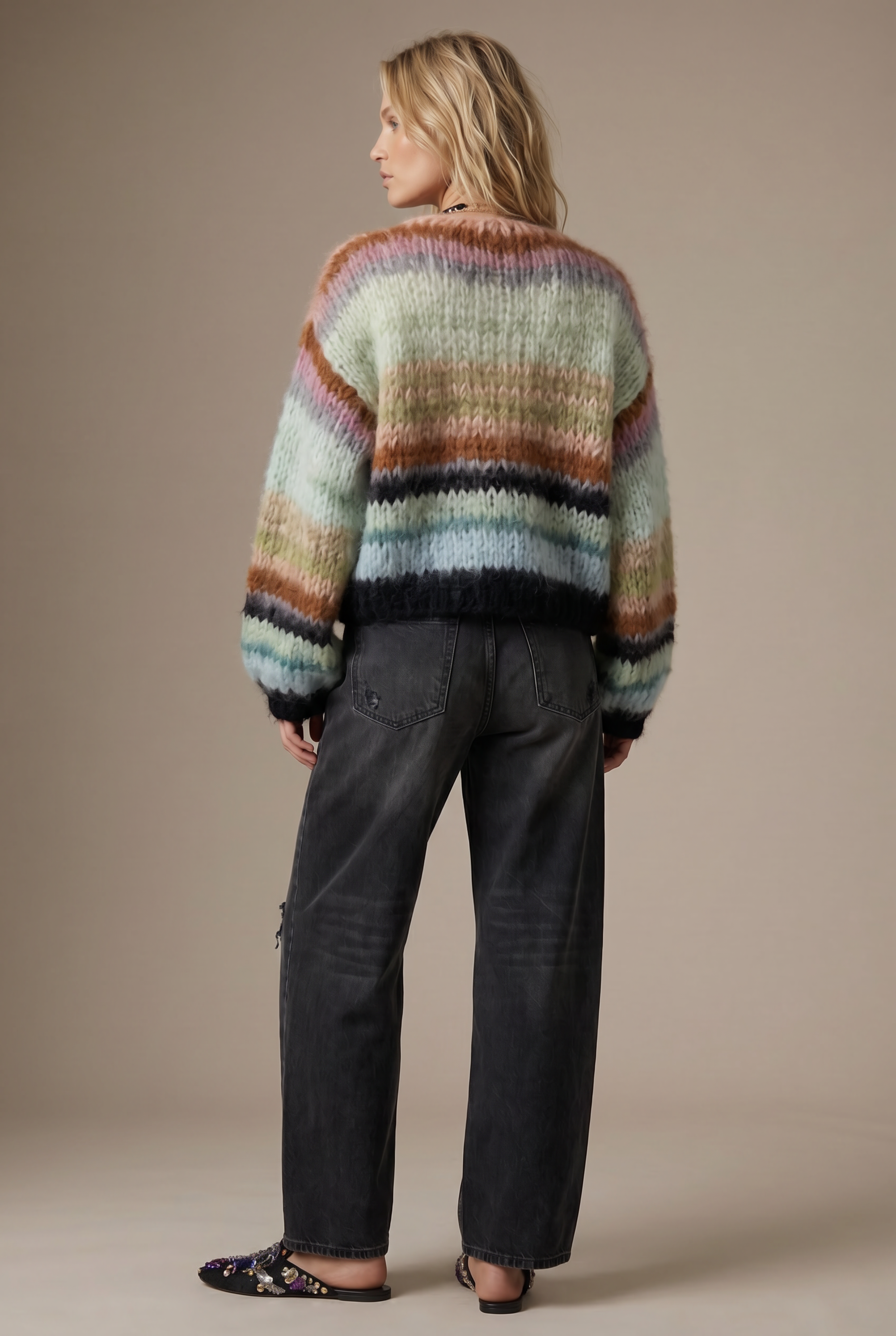 Person wearing a multicolored striped sweater and dark jeans on a beige background