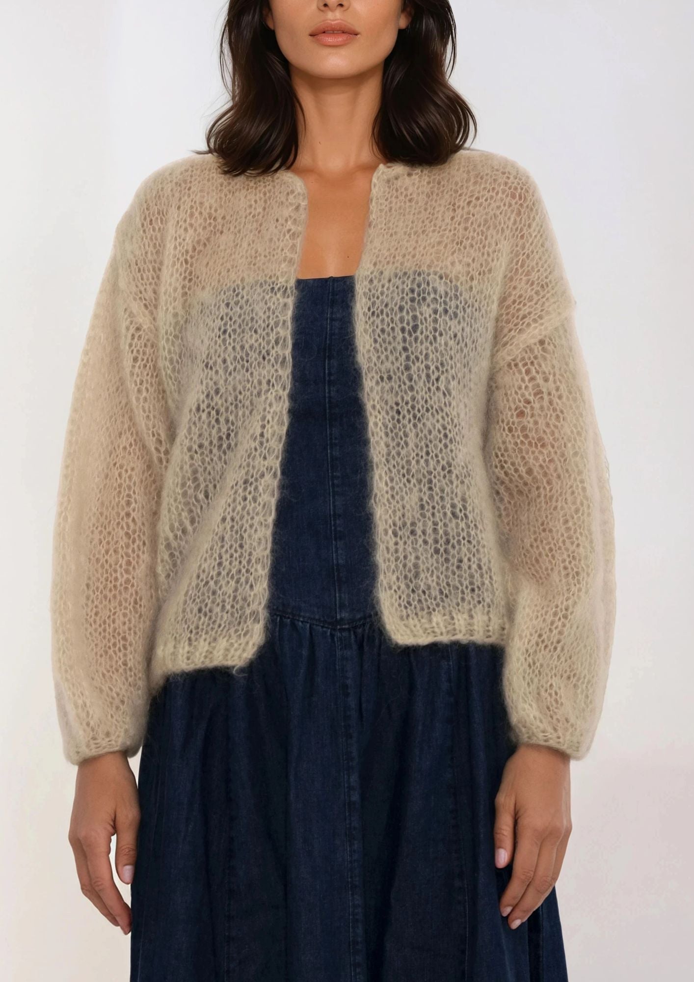 Woman wearing a beige handknitted cardigan over a dark blue dress on a white background