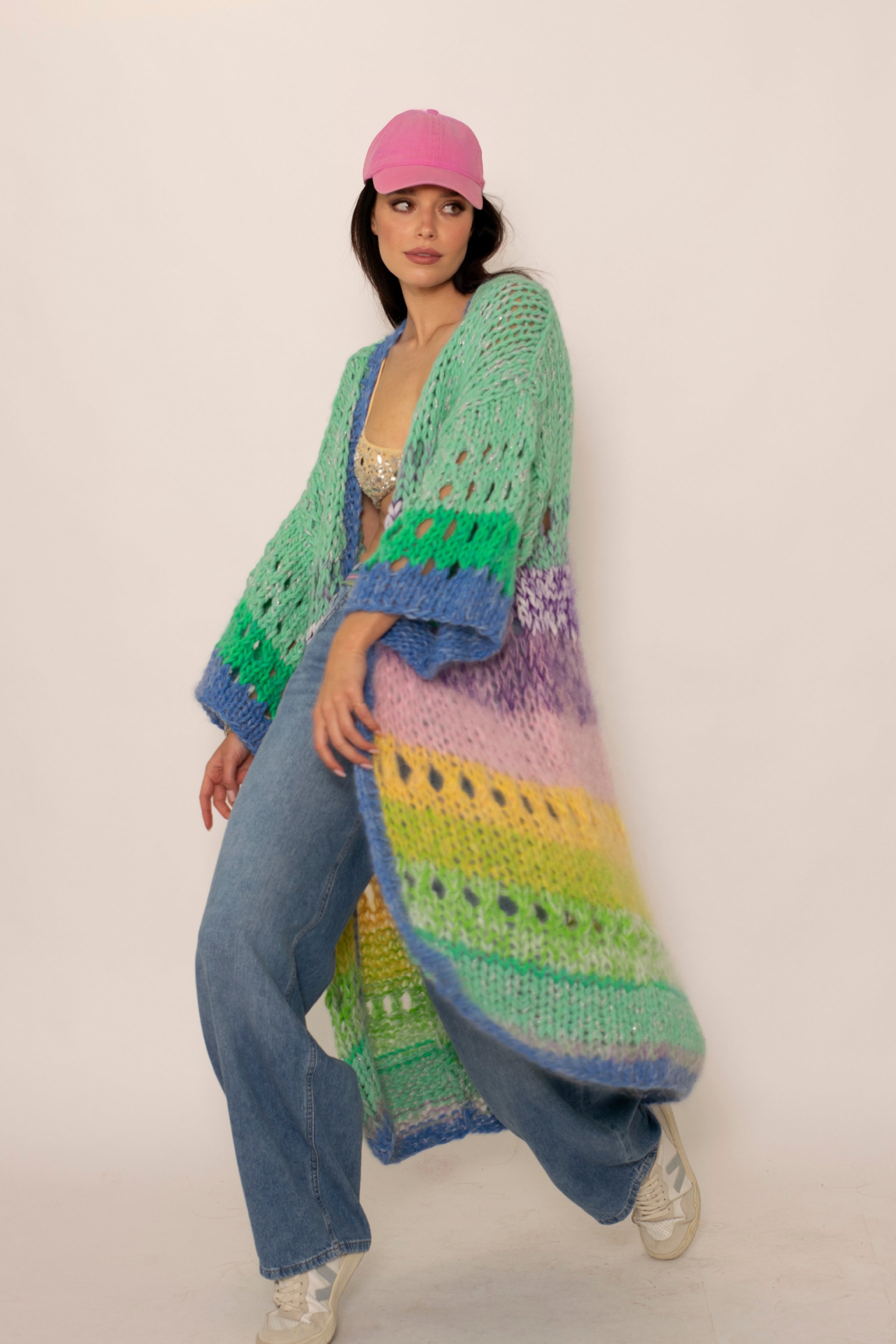 a beautiful woman with a pink cap wearing a colorful pastel striped handknitted cardigan jeans and white sneakers