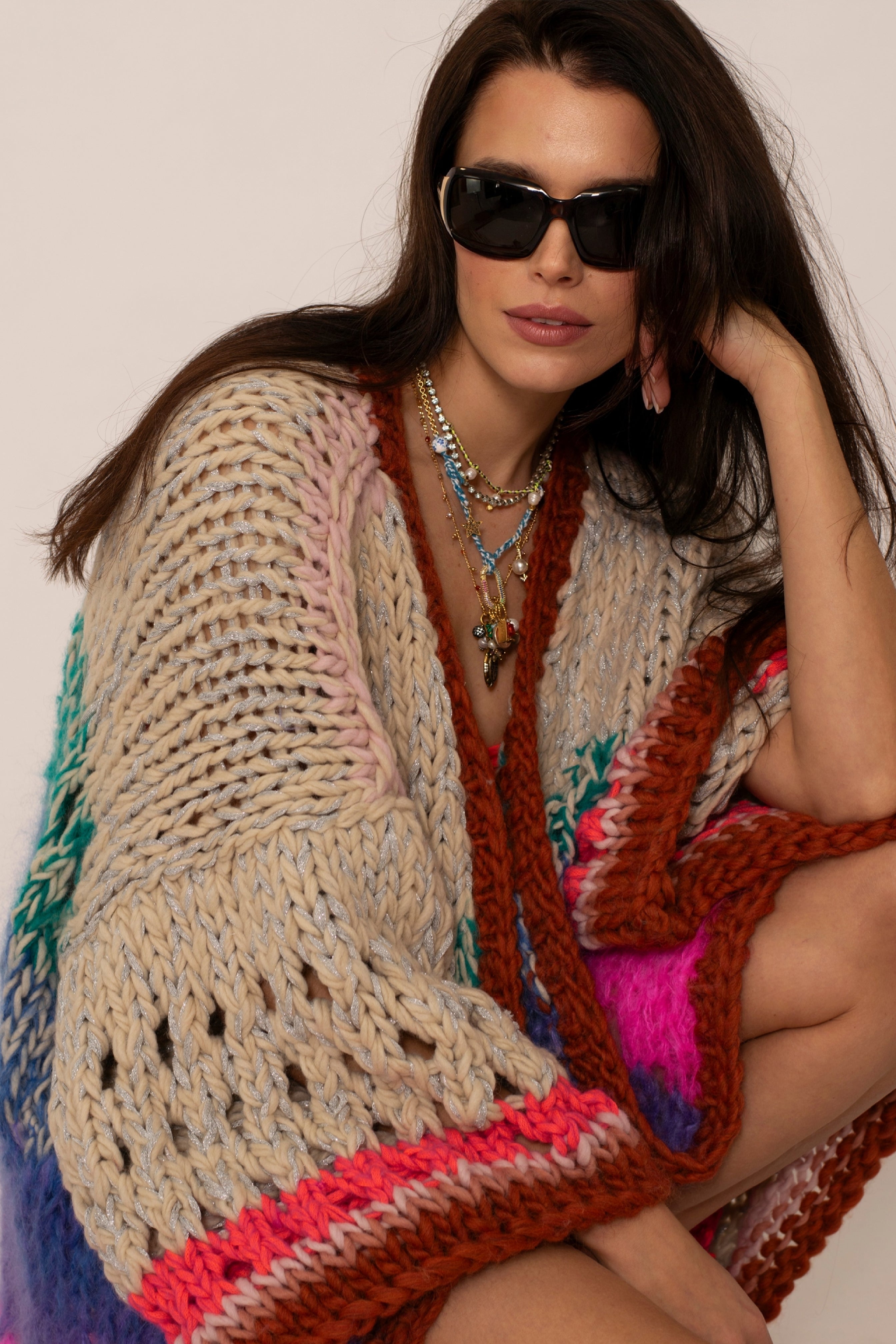 brown hair woman wearing sunglasses and an oversized luxury handknitted cardigan in beige brown and neon colors