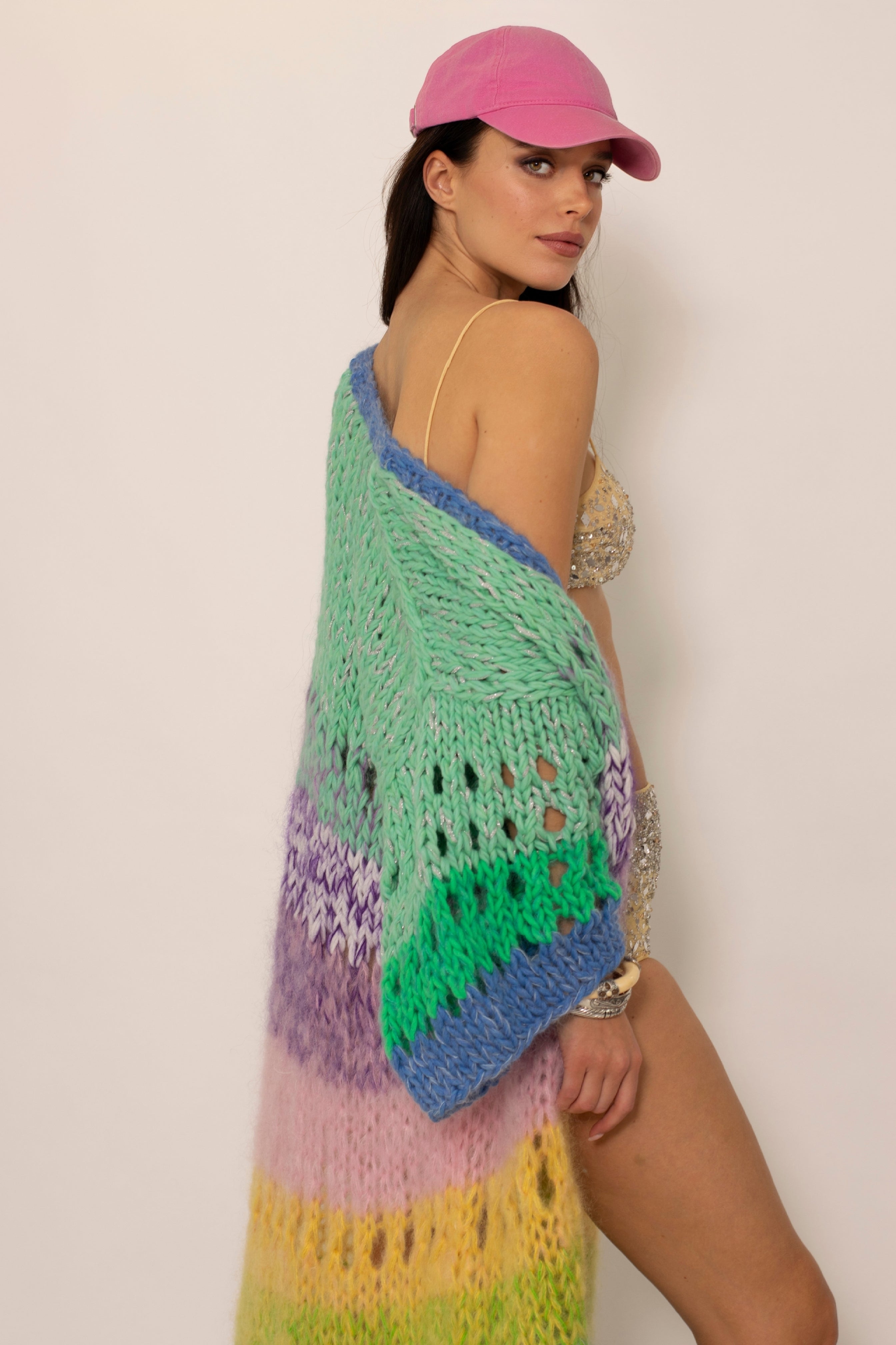 a beautiful girl wearing a pink cap and a colorful pastel striped handknitted cardigan and sequined bikini