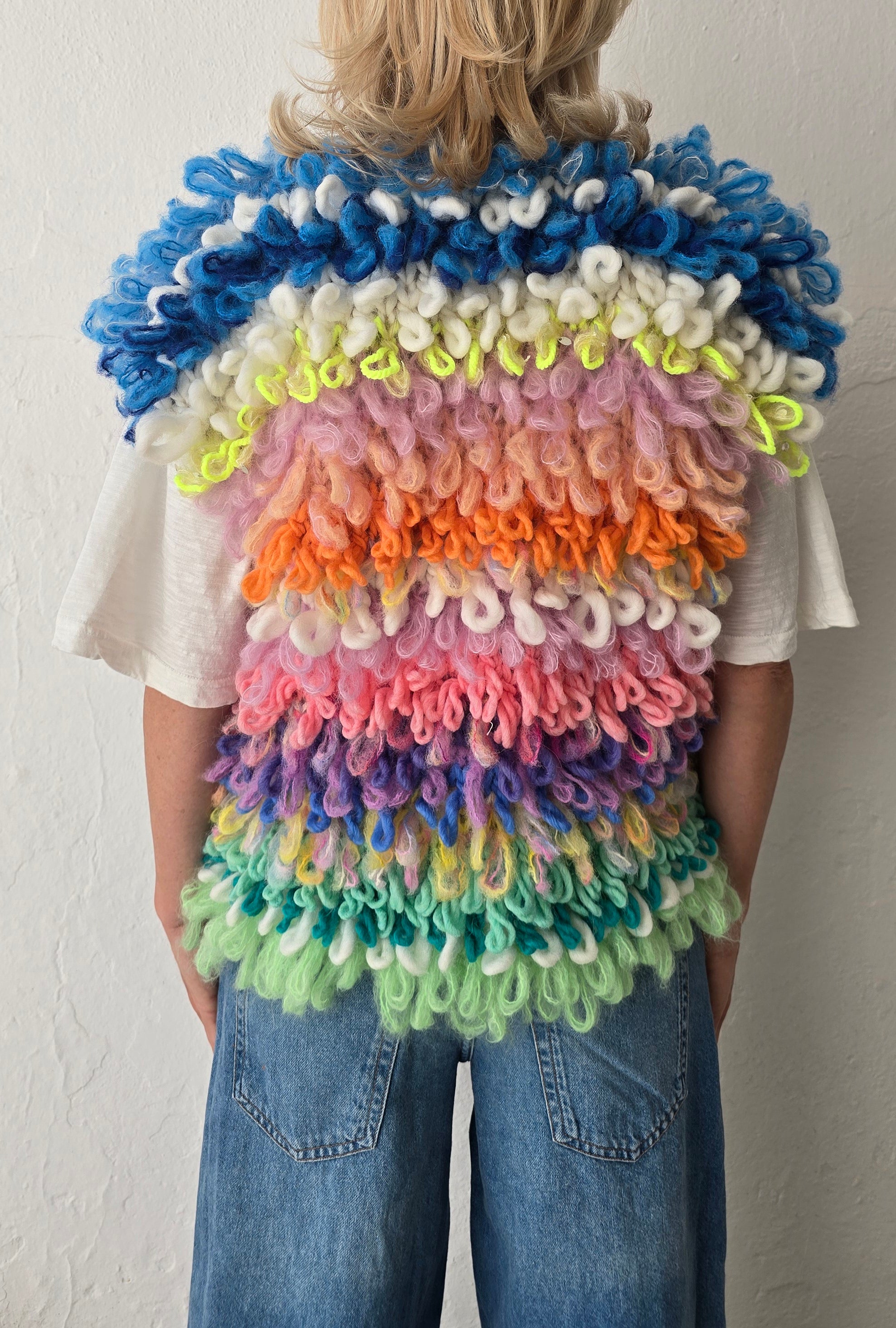 Person wearing a colorful, layered handknit loopstitch vest against a plain background