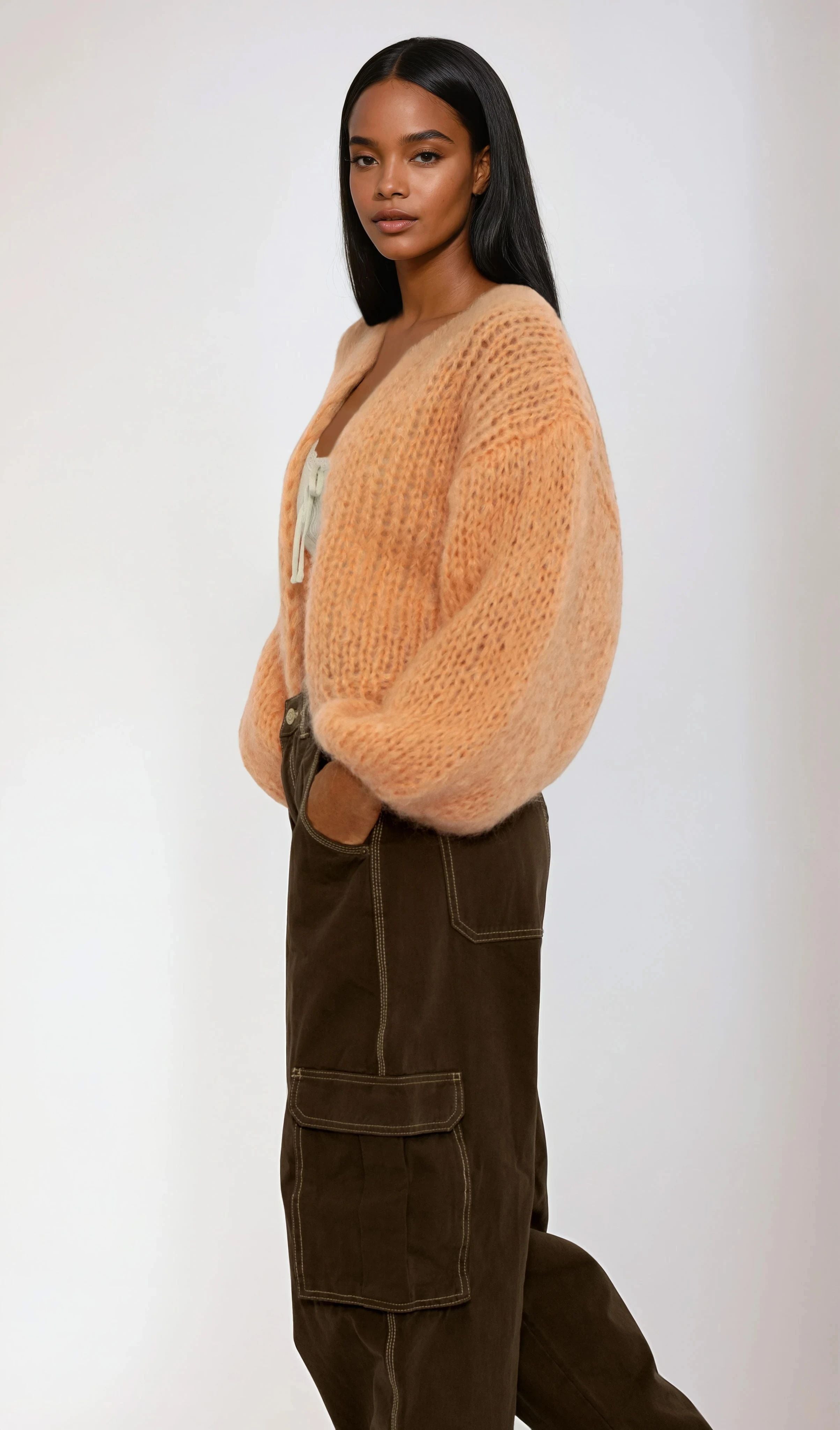 Woman wearing a light orange cardigan and brown pants on a white background