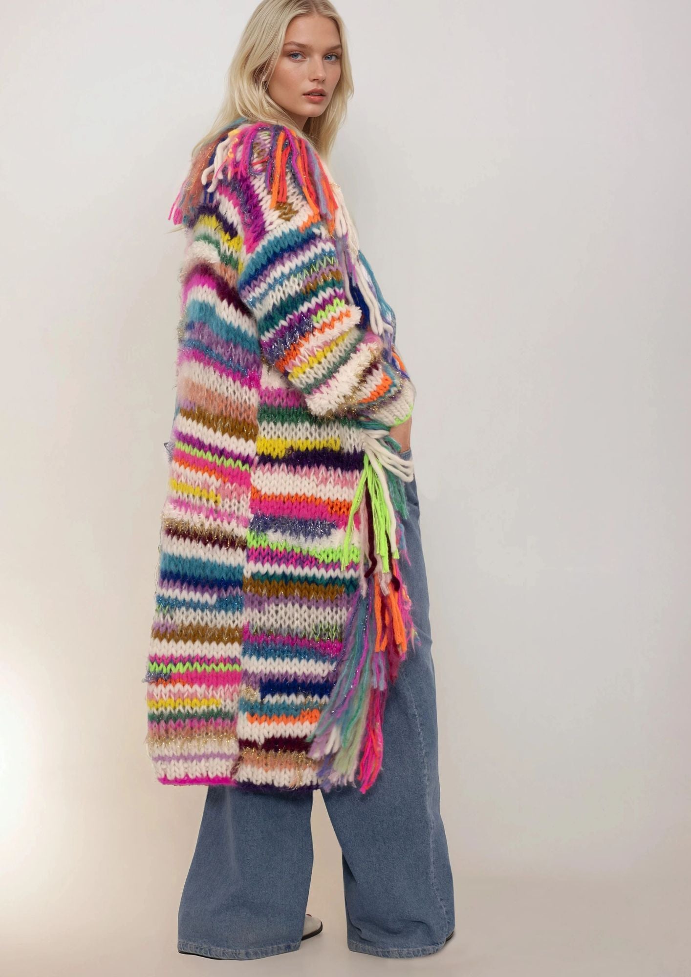 Person wearing a colorful striped handknitted cardigan with tassels on a plain background