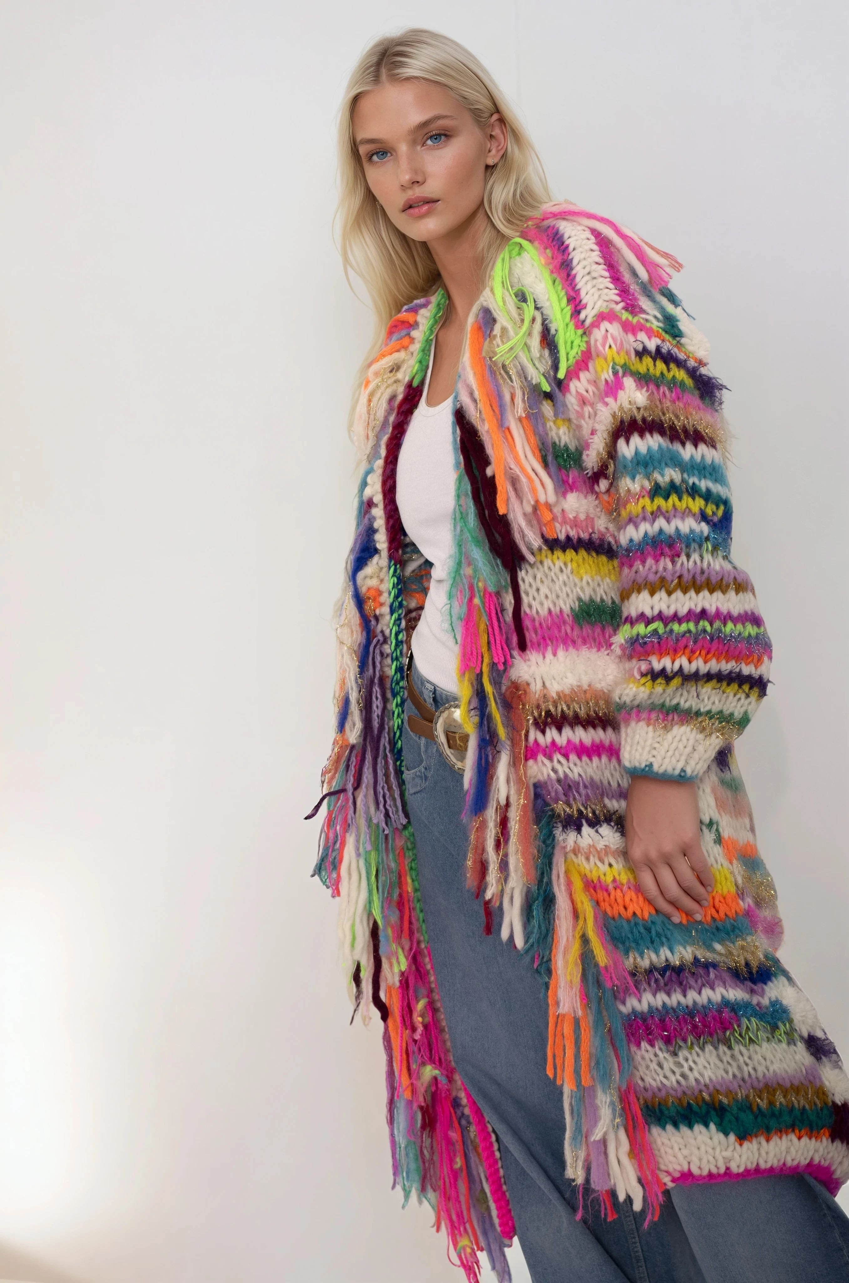 Woman wearing a colorful handknitted cardigan with tassels on a plain background