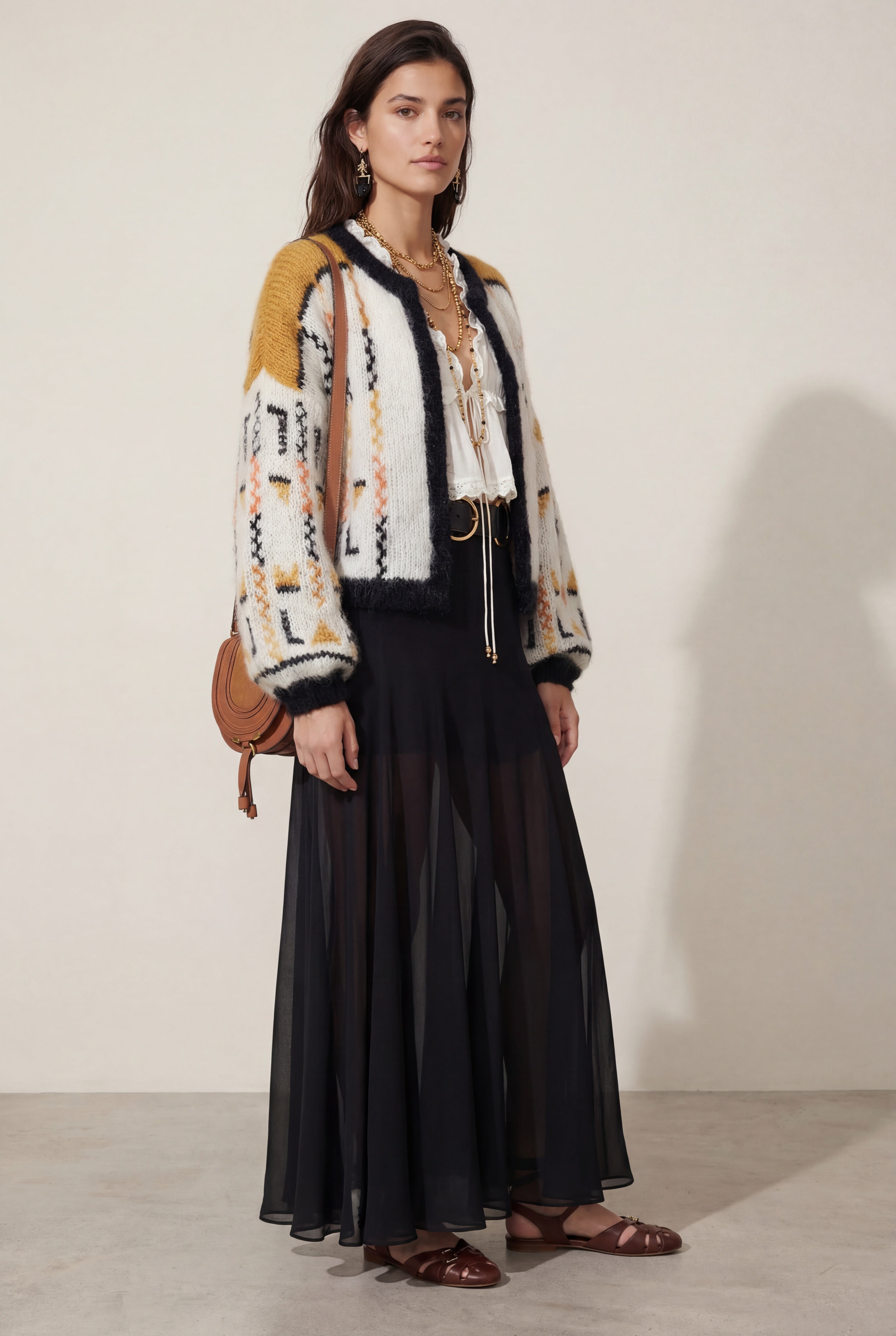 Woman wearing a patterned cardigan, black dress, and brown sandals against a plain background