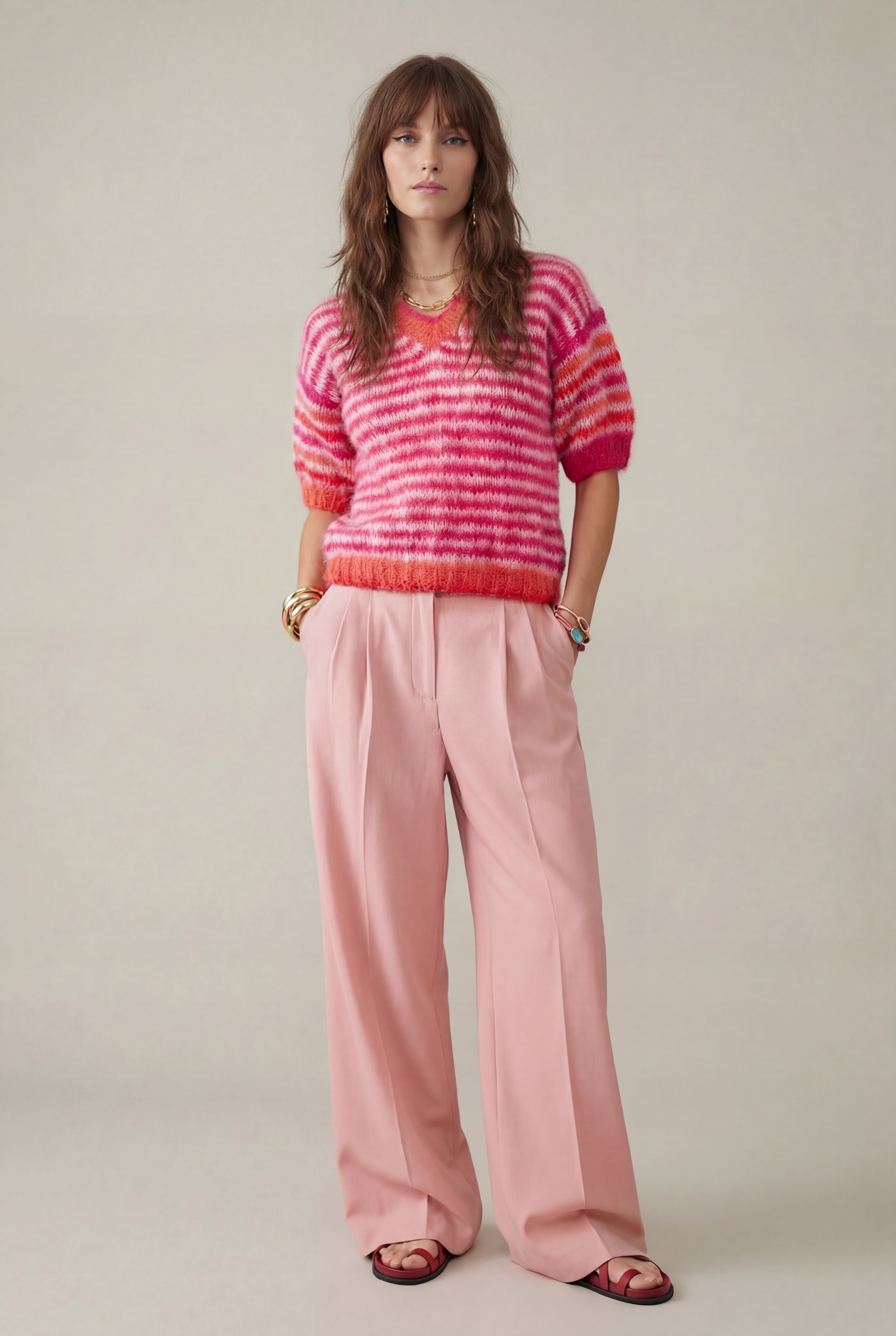 Woman wearing a pink and red striped sweater and pink pants on a plain background