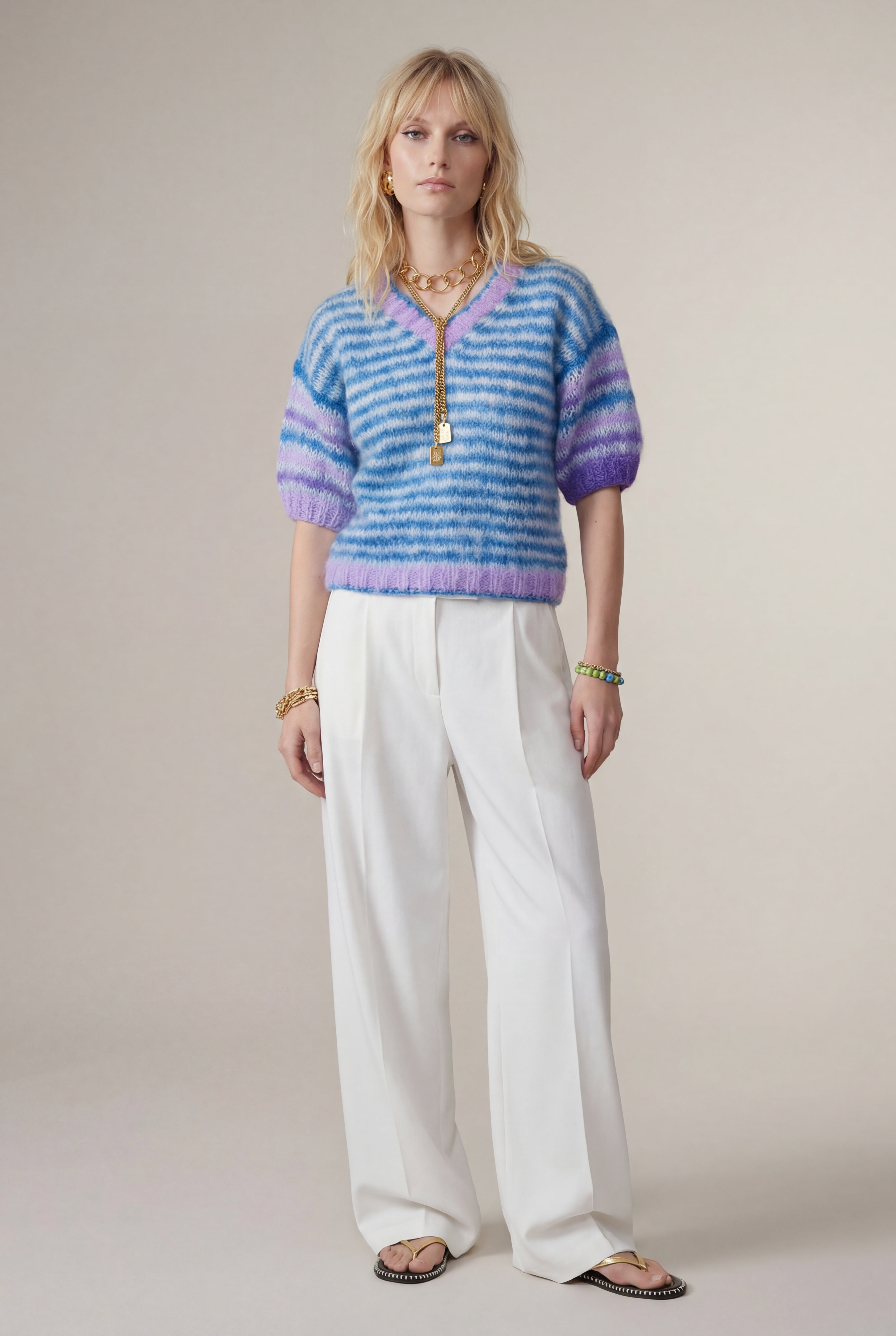 Woman wearing a striped sweater and white pants against a plain background
