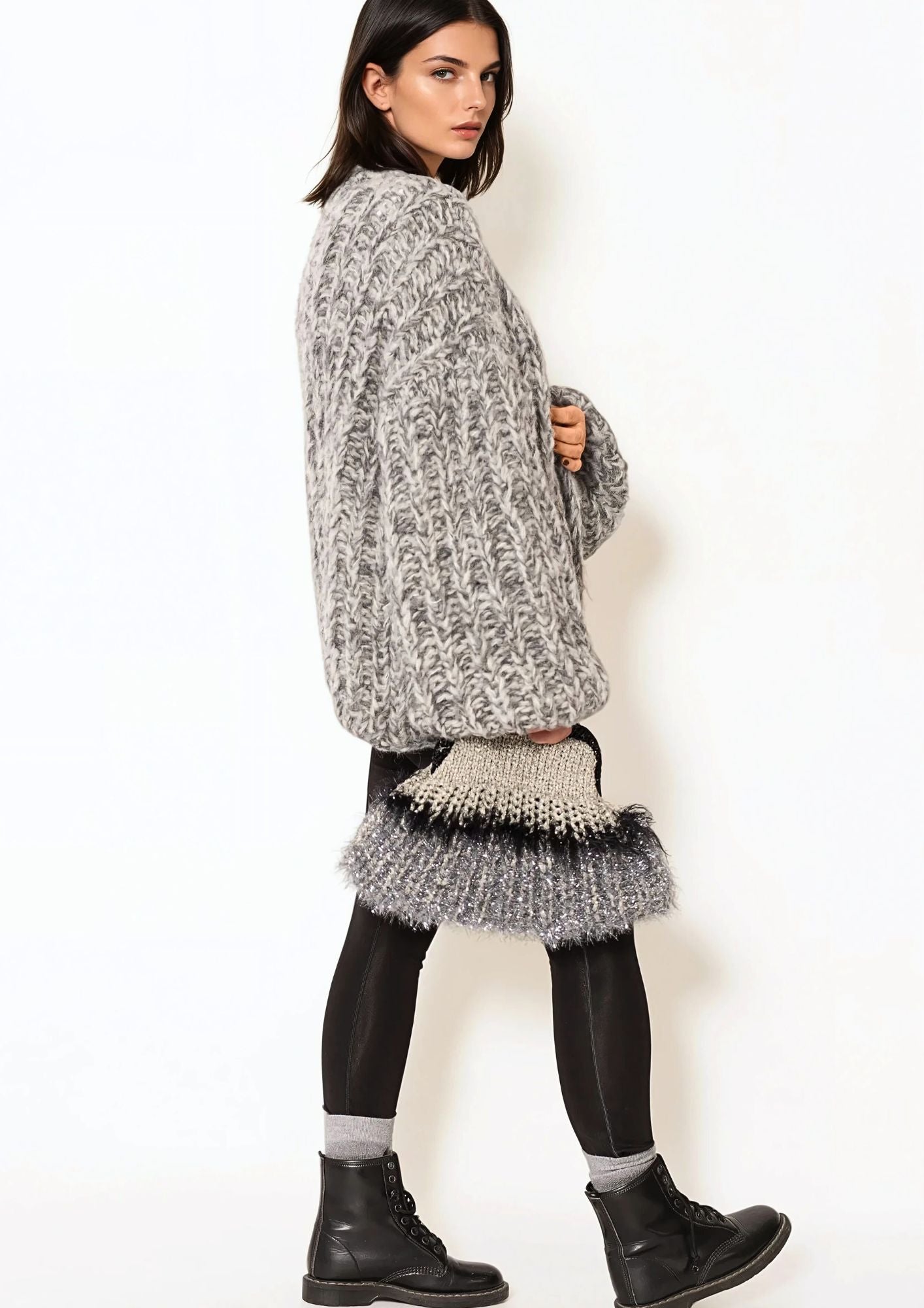 Girl with dark hair in white t shirt and grey melange handknitted oversized luxury mohair cardigan nad handcrocheted clutch, lack leggings and black cool boots