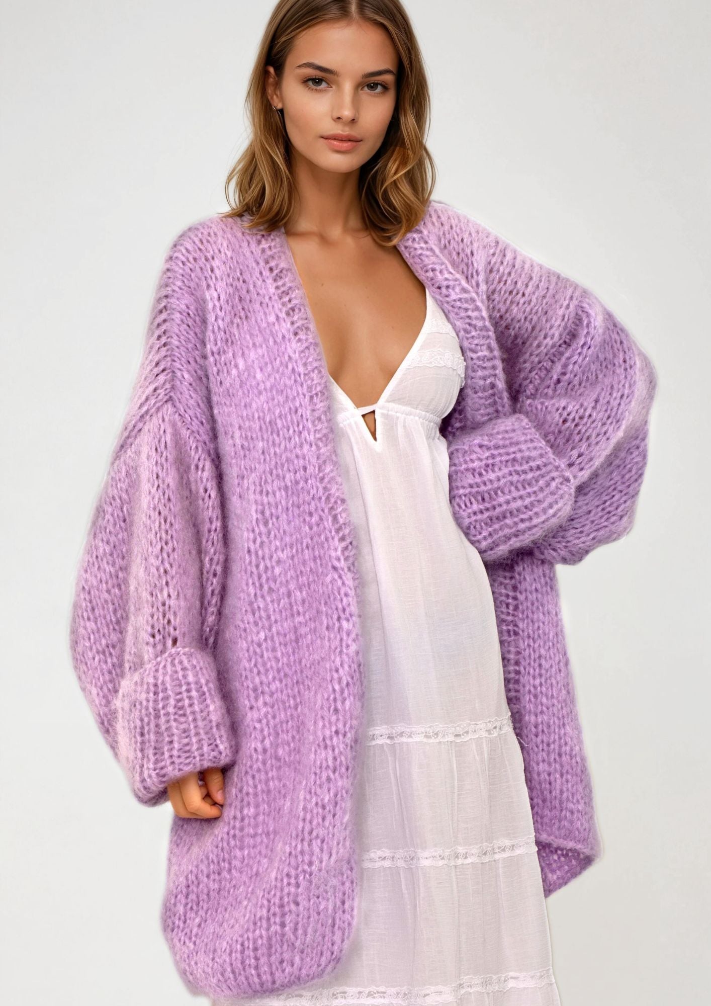Woman wearing a purple cardigan over a white dress on a plain background