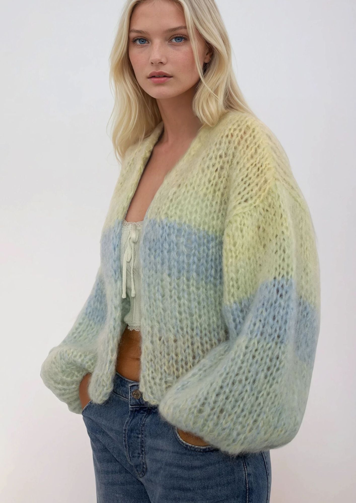 Woman wearing a degrade light green and blue striped handknitted sweater against a white background