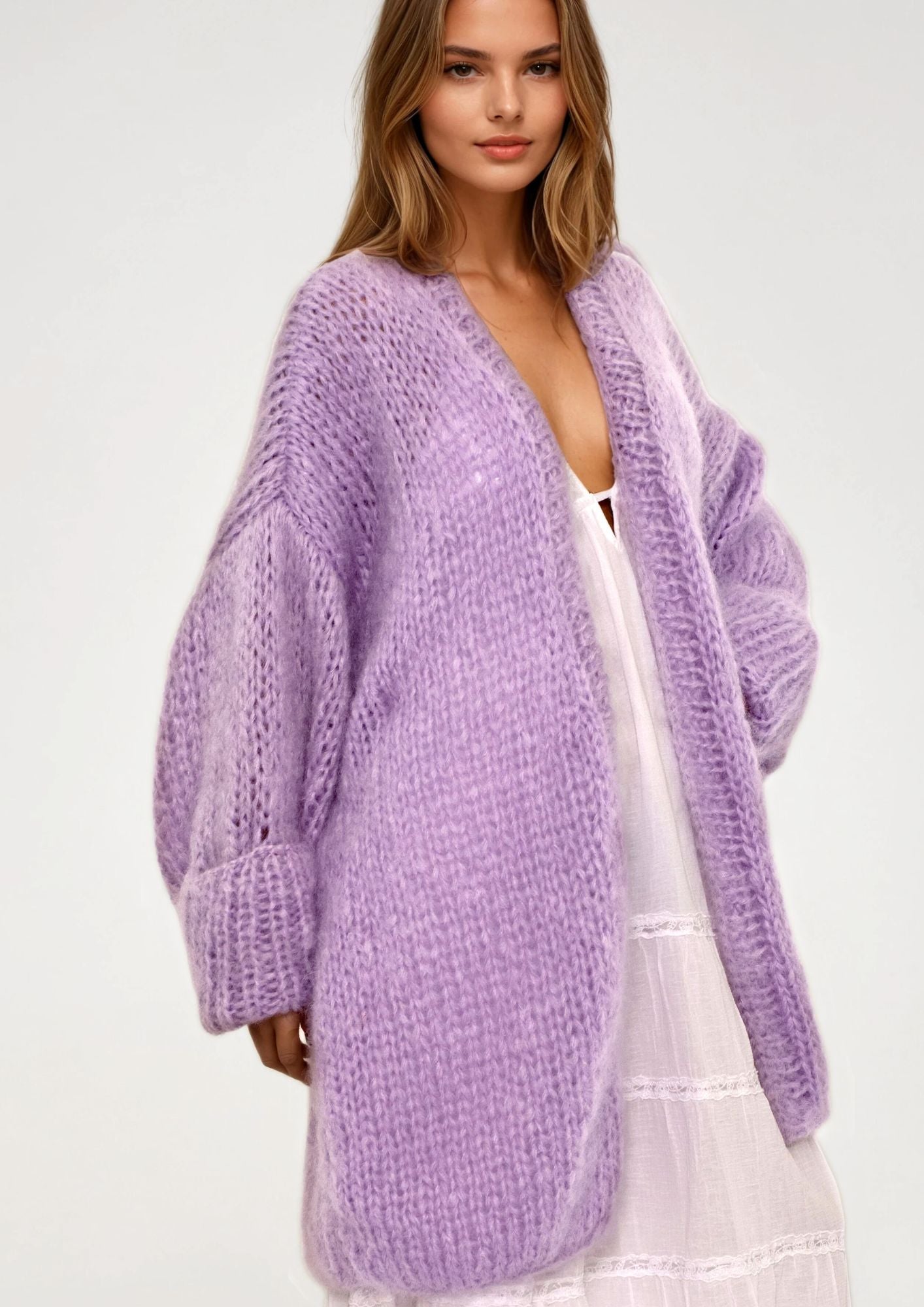 Woman wearing a purple cardigan over a white dress on a plain background