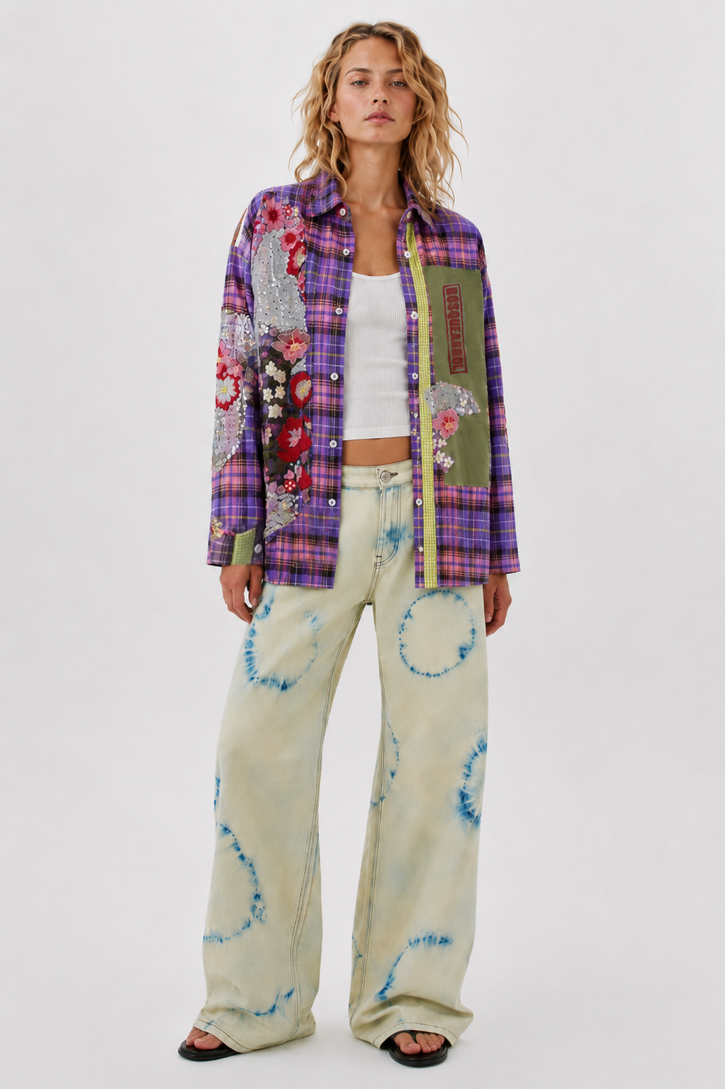 Woman wearing a colorful patchwork jacket and patterned pants on a white background