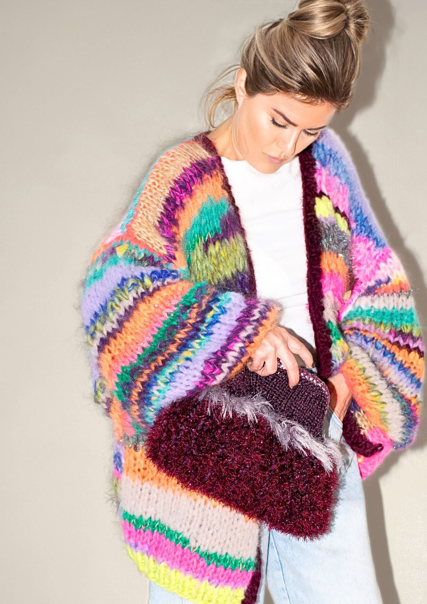 a blonde woman with striped colorful cardigna with burgundy clutch bag