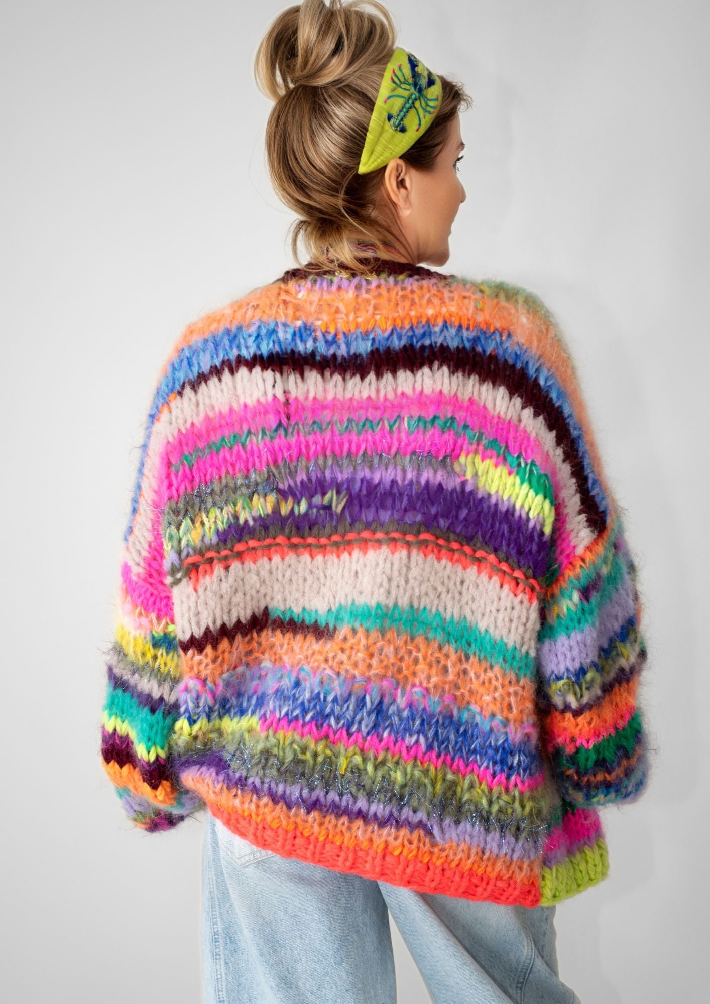 back of a blonde woman with a handknitted striped colorful cardigan  and jeans