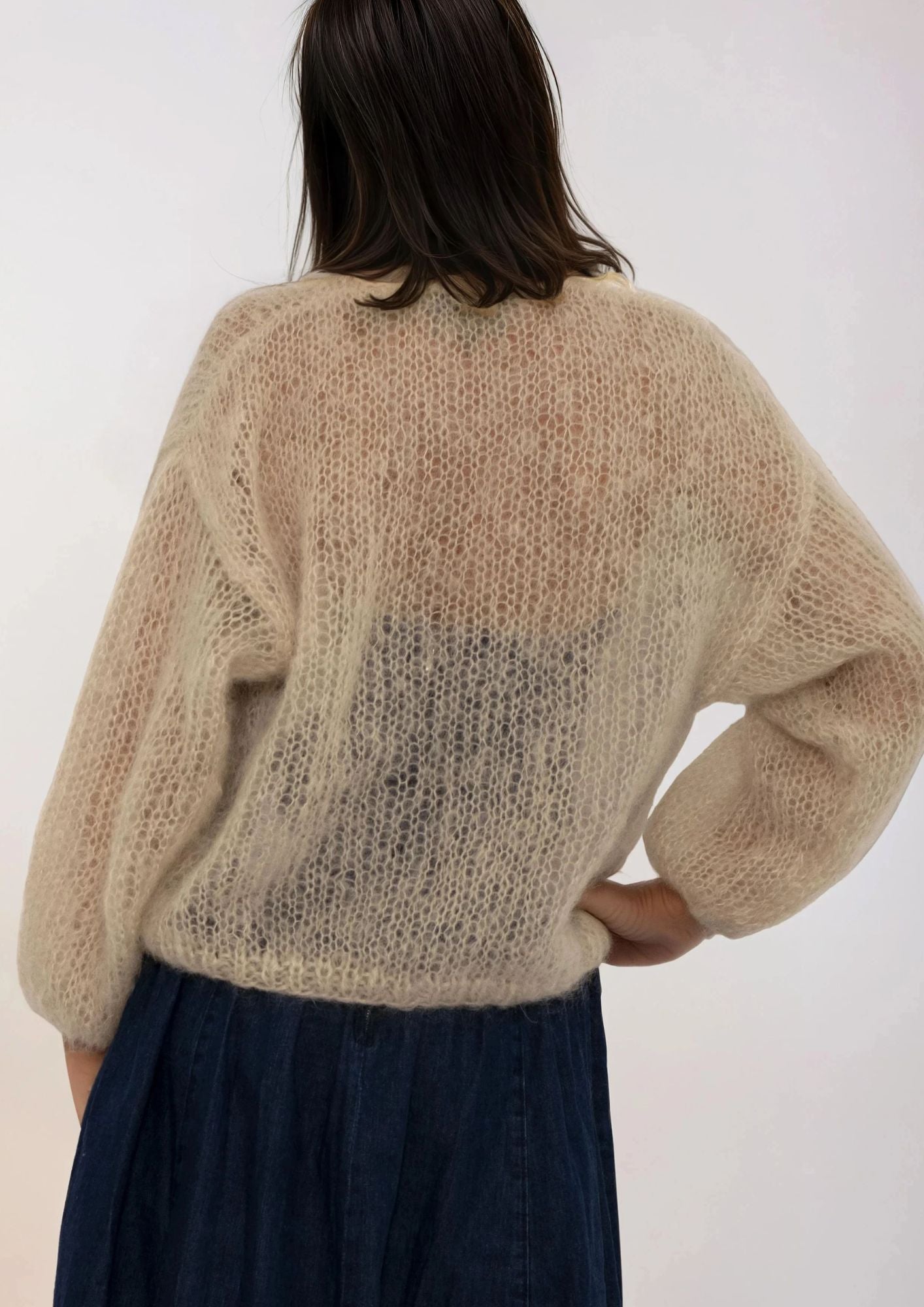 Person wearing a beige handmade sweater with a white background
