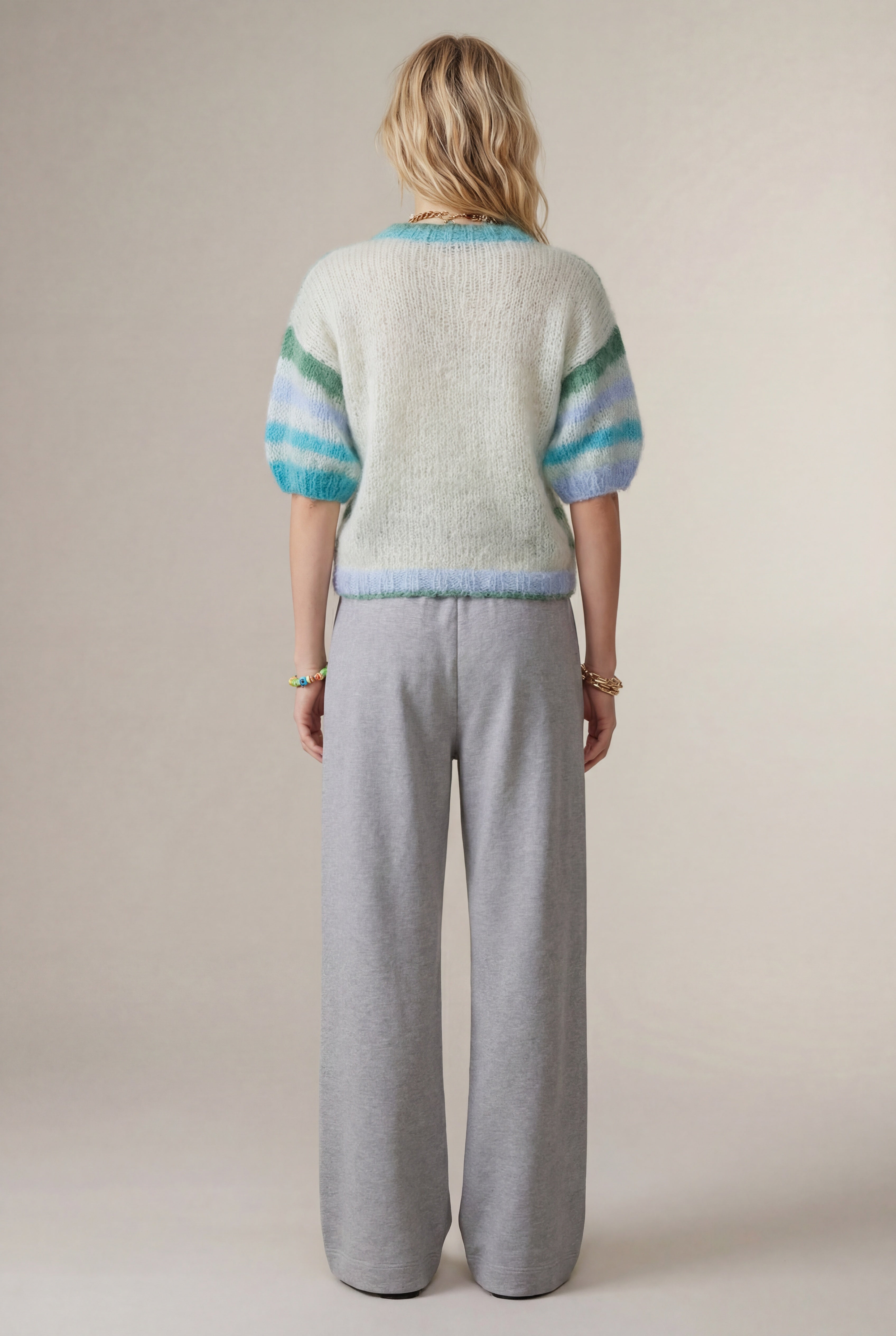 Person wearing a light-colored sweater with blue and green stripes and gray Dries van Noten pants on a plain background
