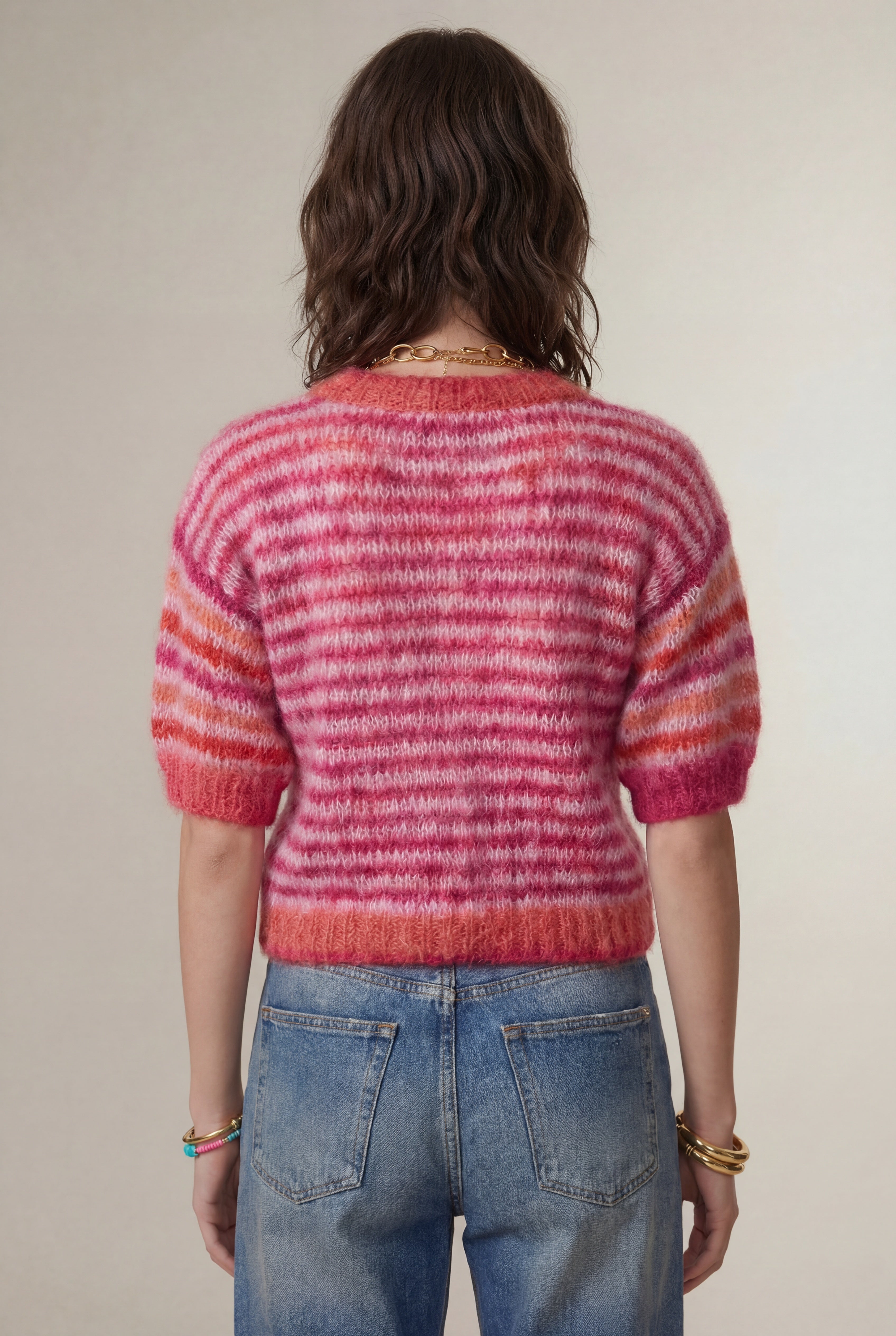 Person wearing a pink and red striped sweater and blue jeans backview against a plain background