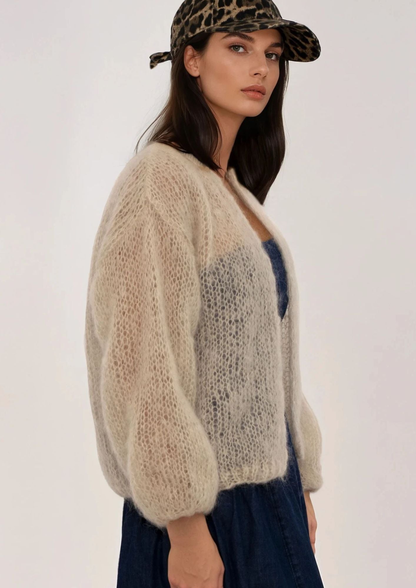 Woman wearing a beige handknitted cardigan and leopard print cap on a white background