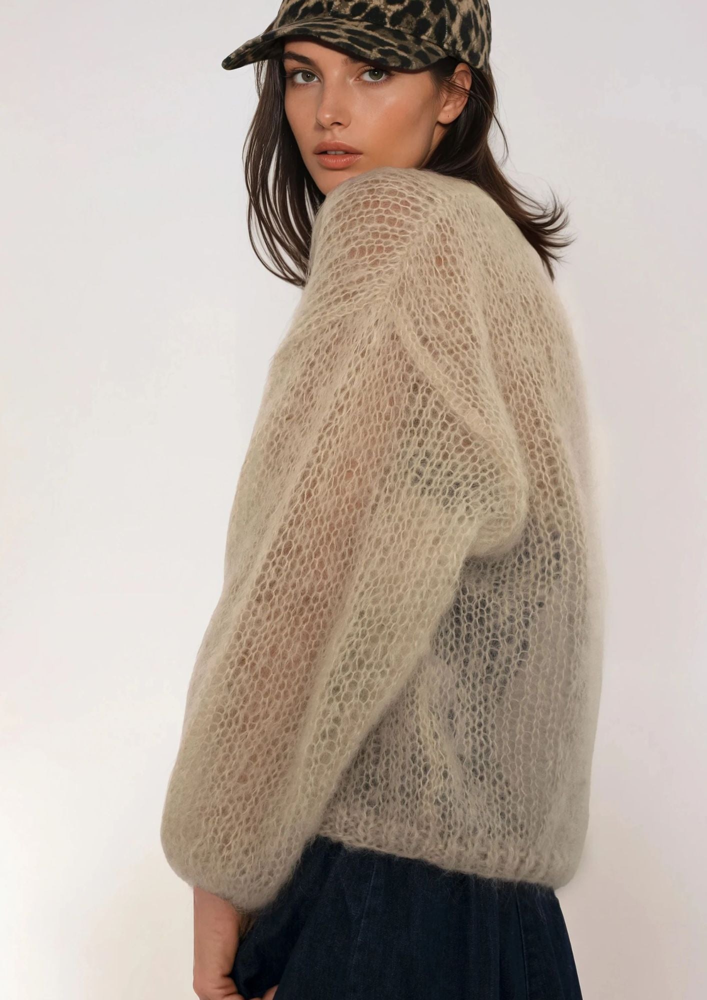 Woman wearing a beige handknitted sweater and leopard print cap against a white background