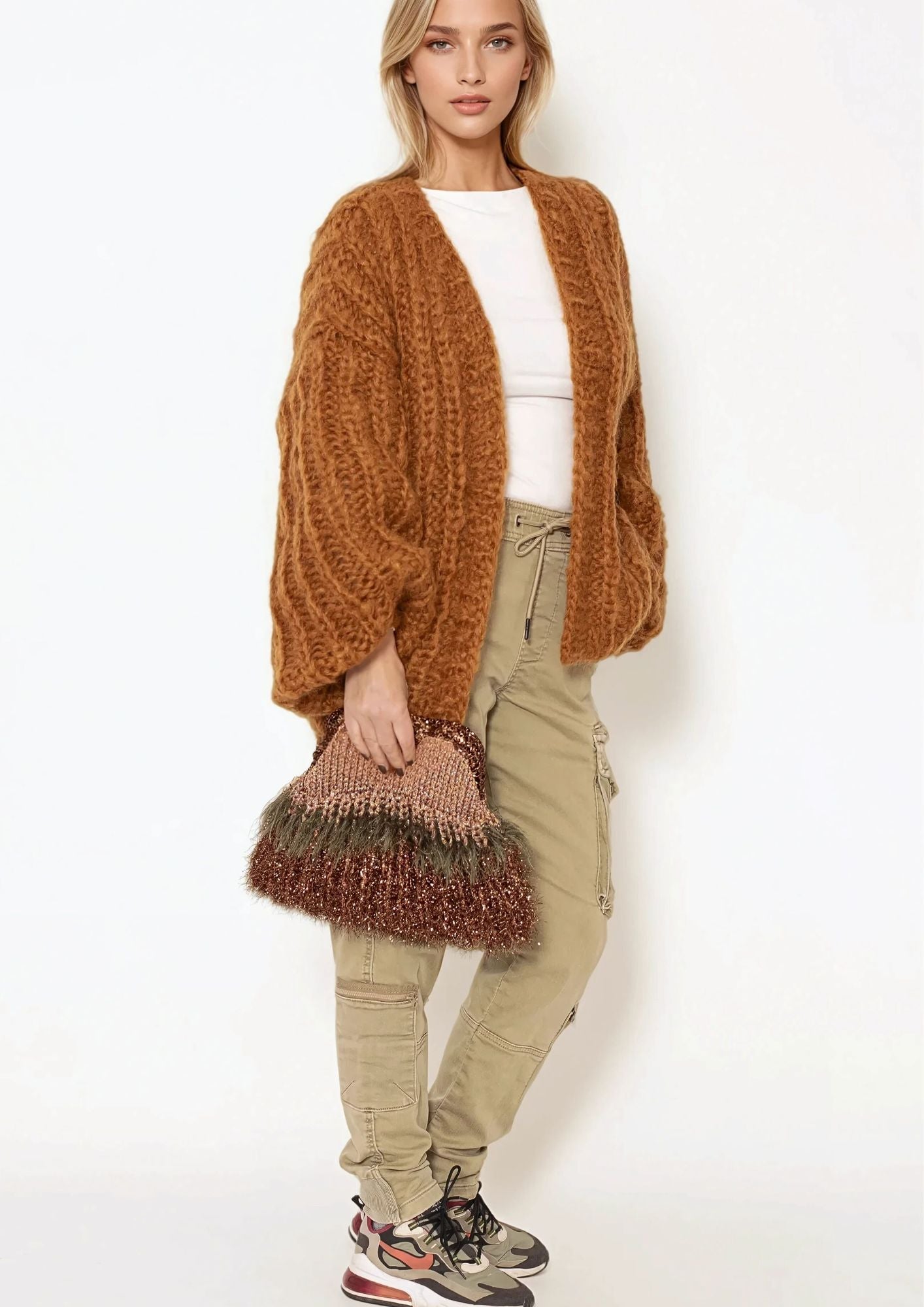 blonde girl in handknitted chunky cardigan in brown ,khaki pants and brown green nadia dafri clutch