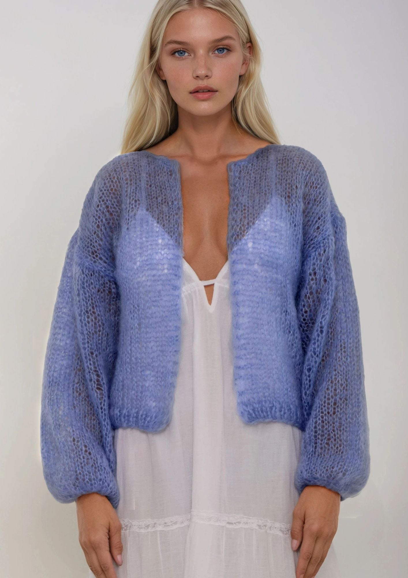 Woman wearing a blue handknitted cardigan over a white dress on a plain background