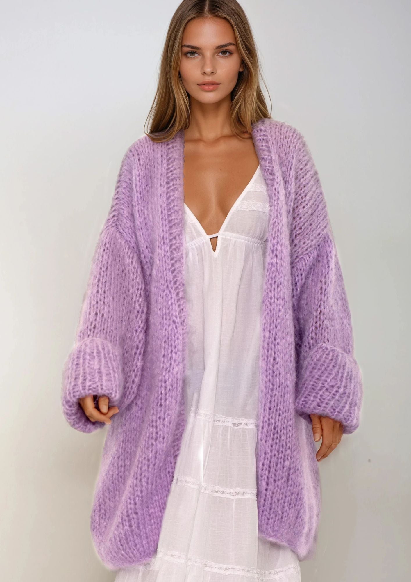 Woman wearing a light purple cardigan over a white dress against a plain background