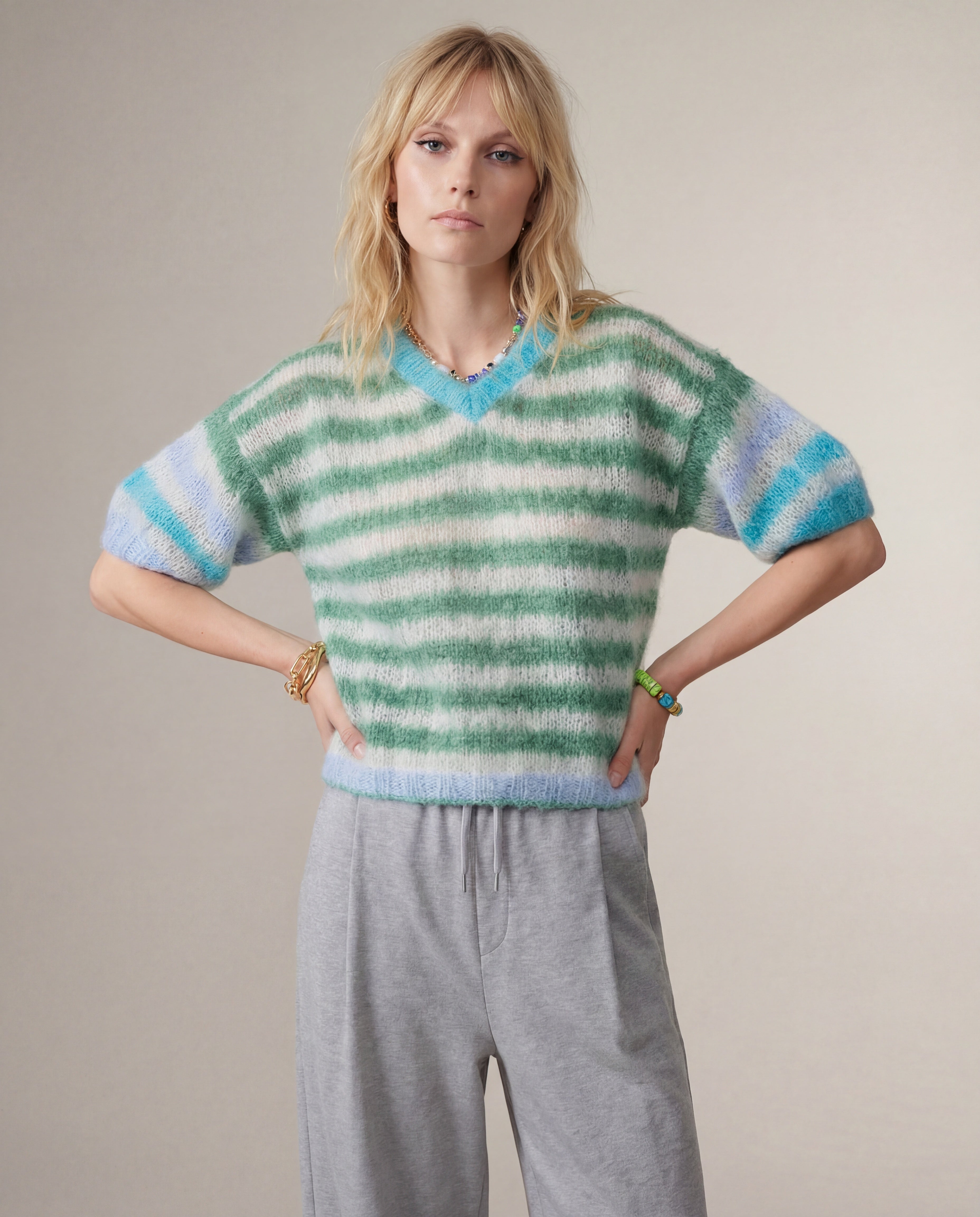 Woman wearing a green and blue striped sweater with gray pants on a plain background