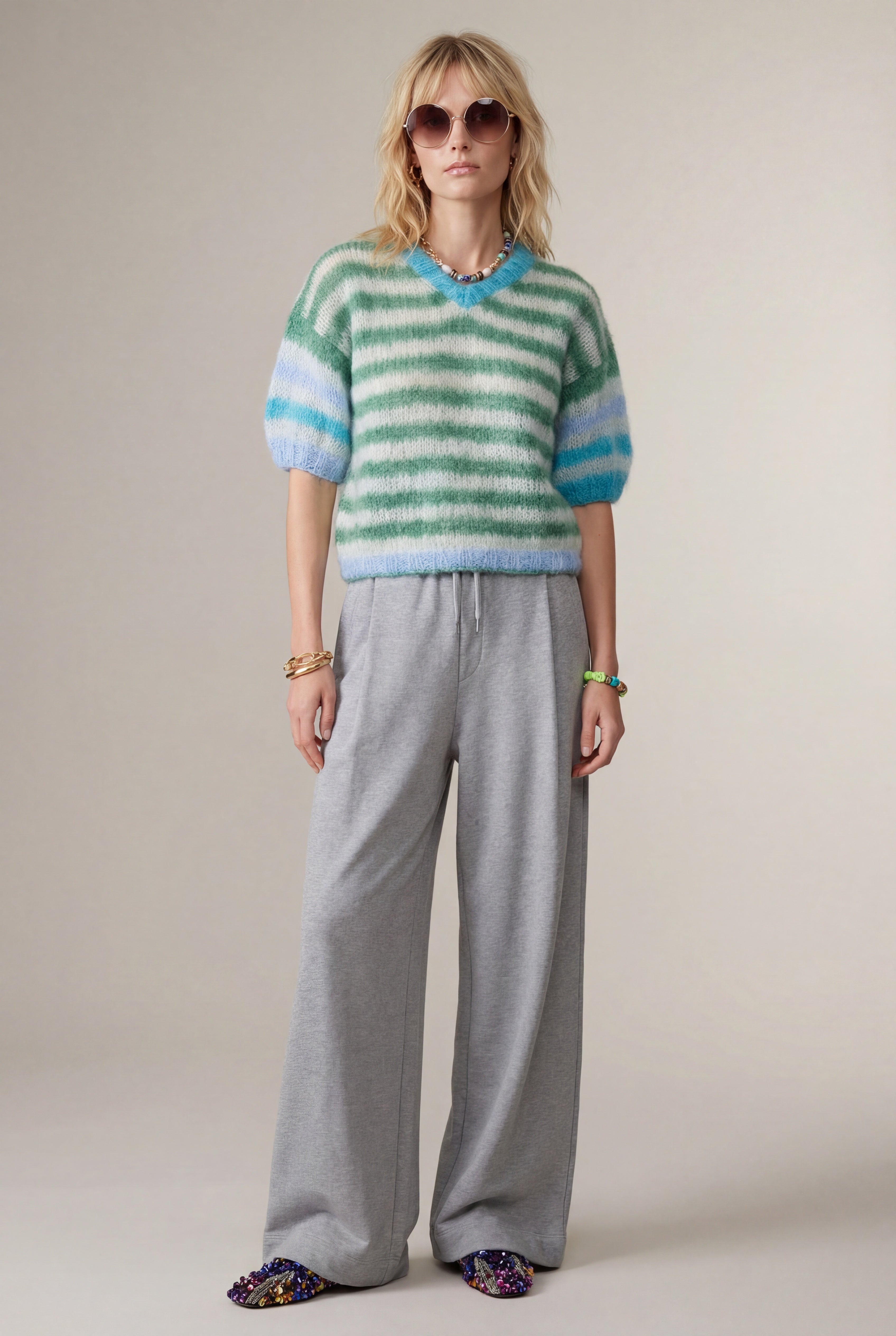 Woman wearing a striped sweater and gray pants against a plain background