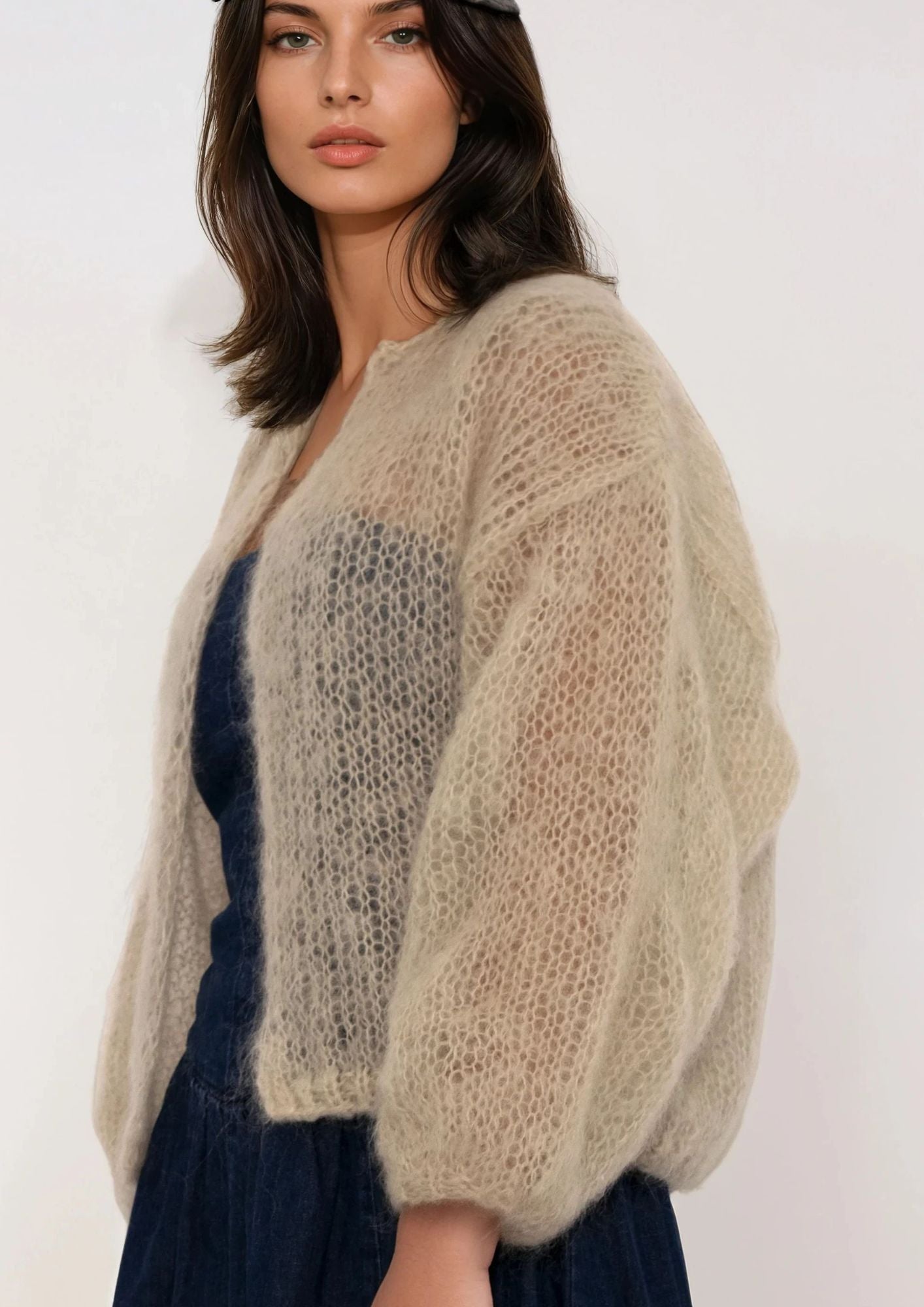 Woman wearing a beige handknitted cardigan over a dark blue dress on a white background