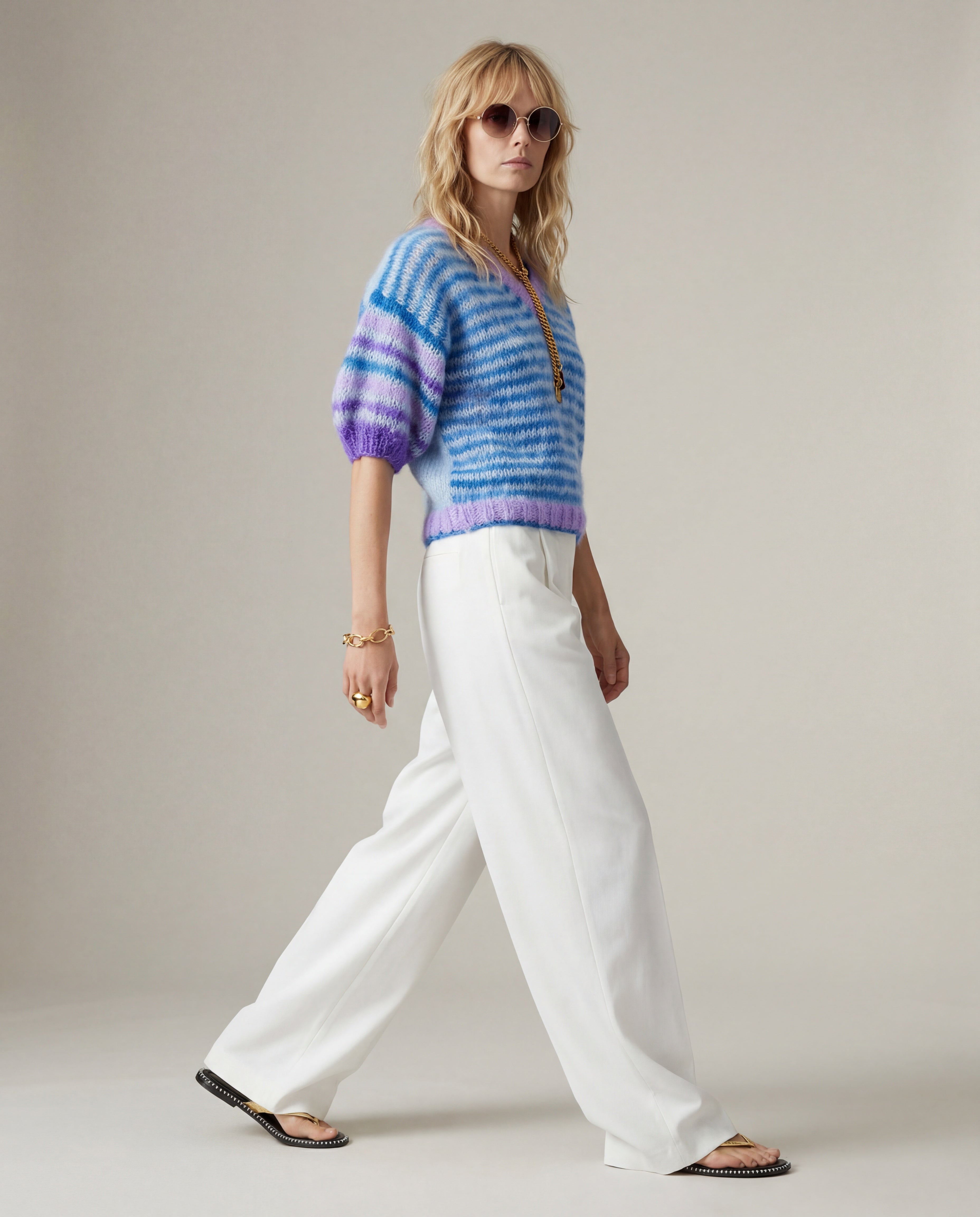 Woman wearing a colorful knitted sweater and white pants on a plain background