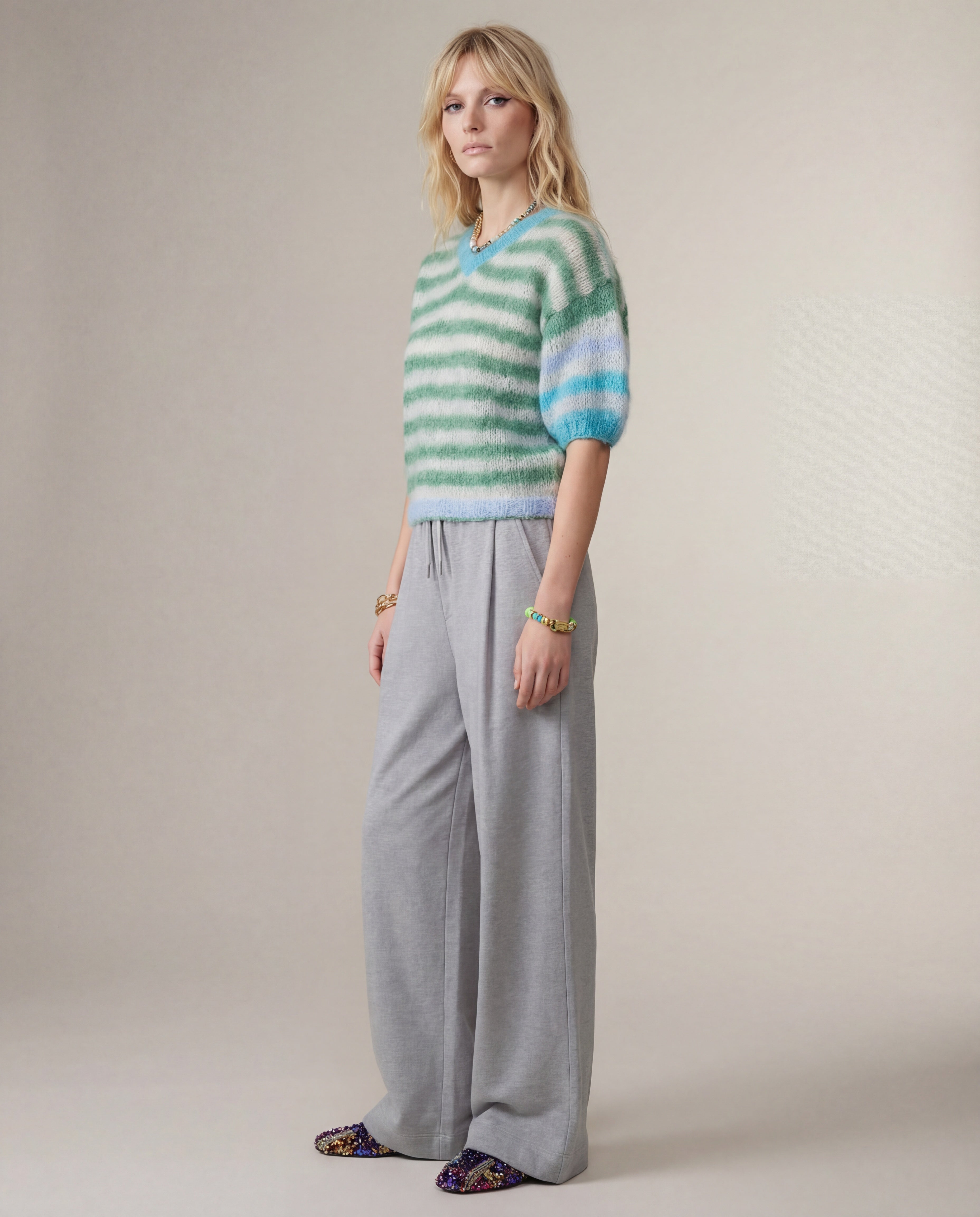 Woman wearing a striped sweater and gray pants against a plain background