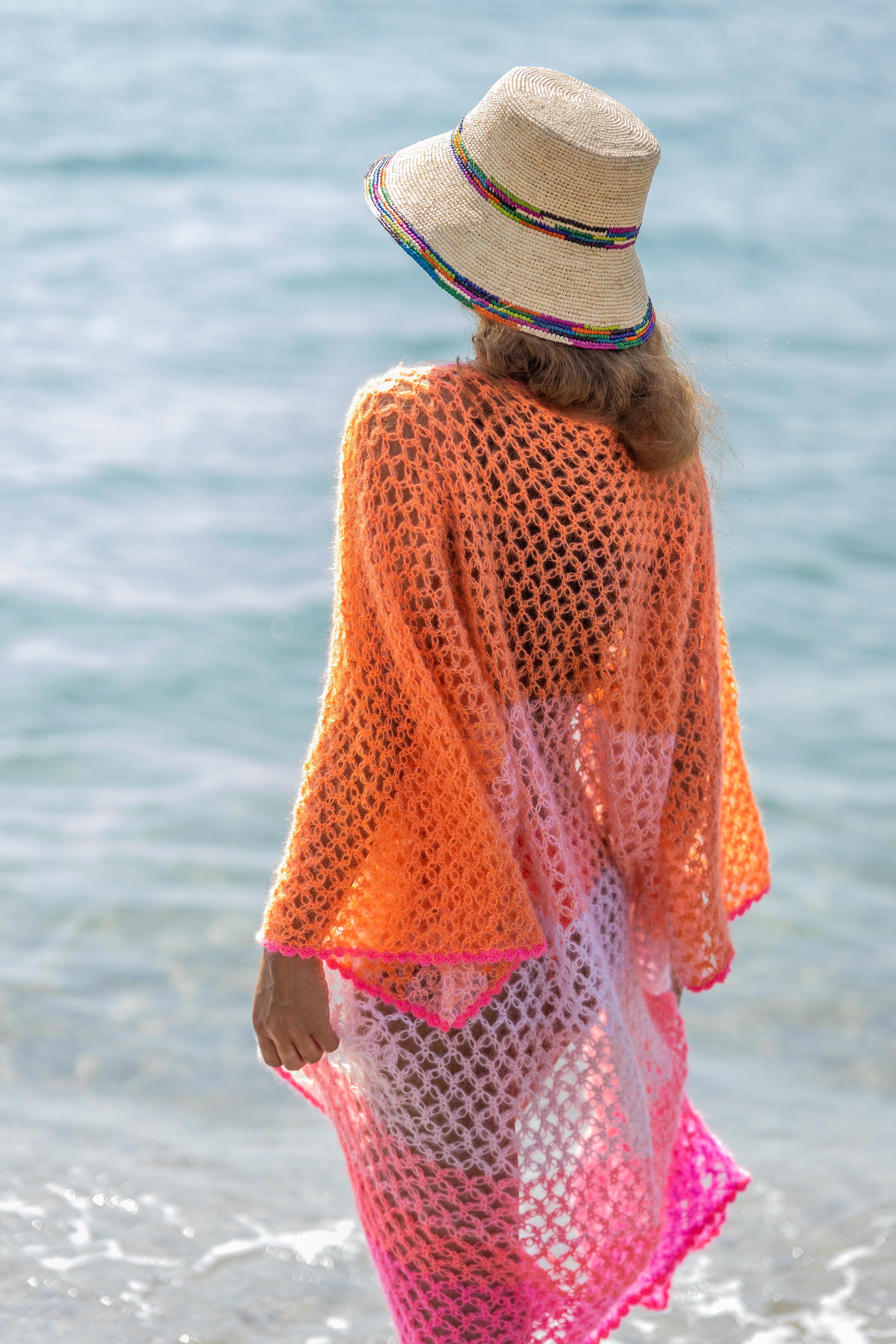 Woman on the beach in a handcrocheted kimono in orange pink