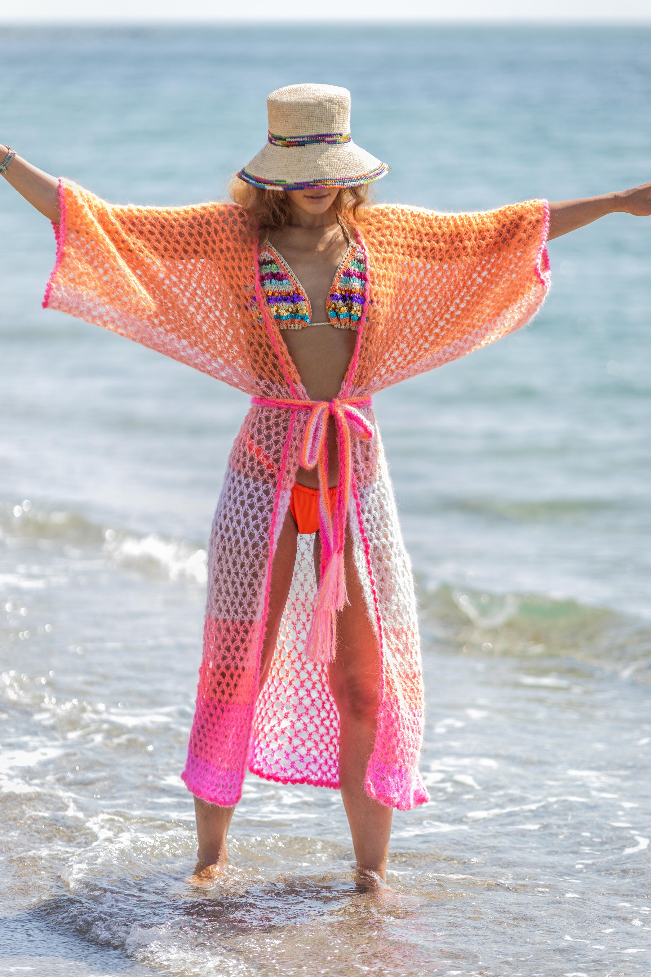 Woman on the beach in a handcrocheted kimono in orange pink