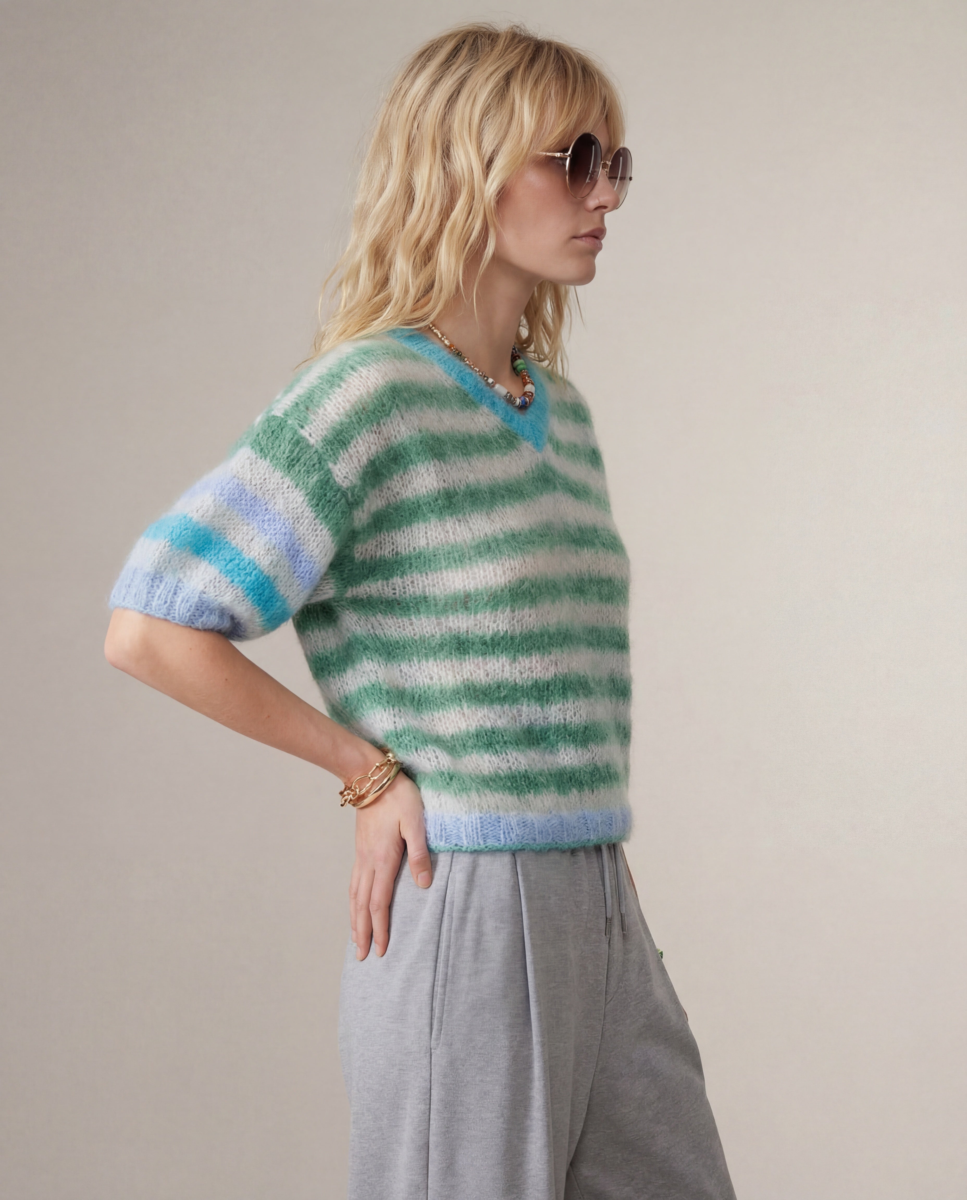 Woman wearing a green and blue striped sweater with gray pants against a plain background